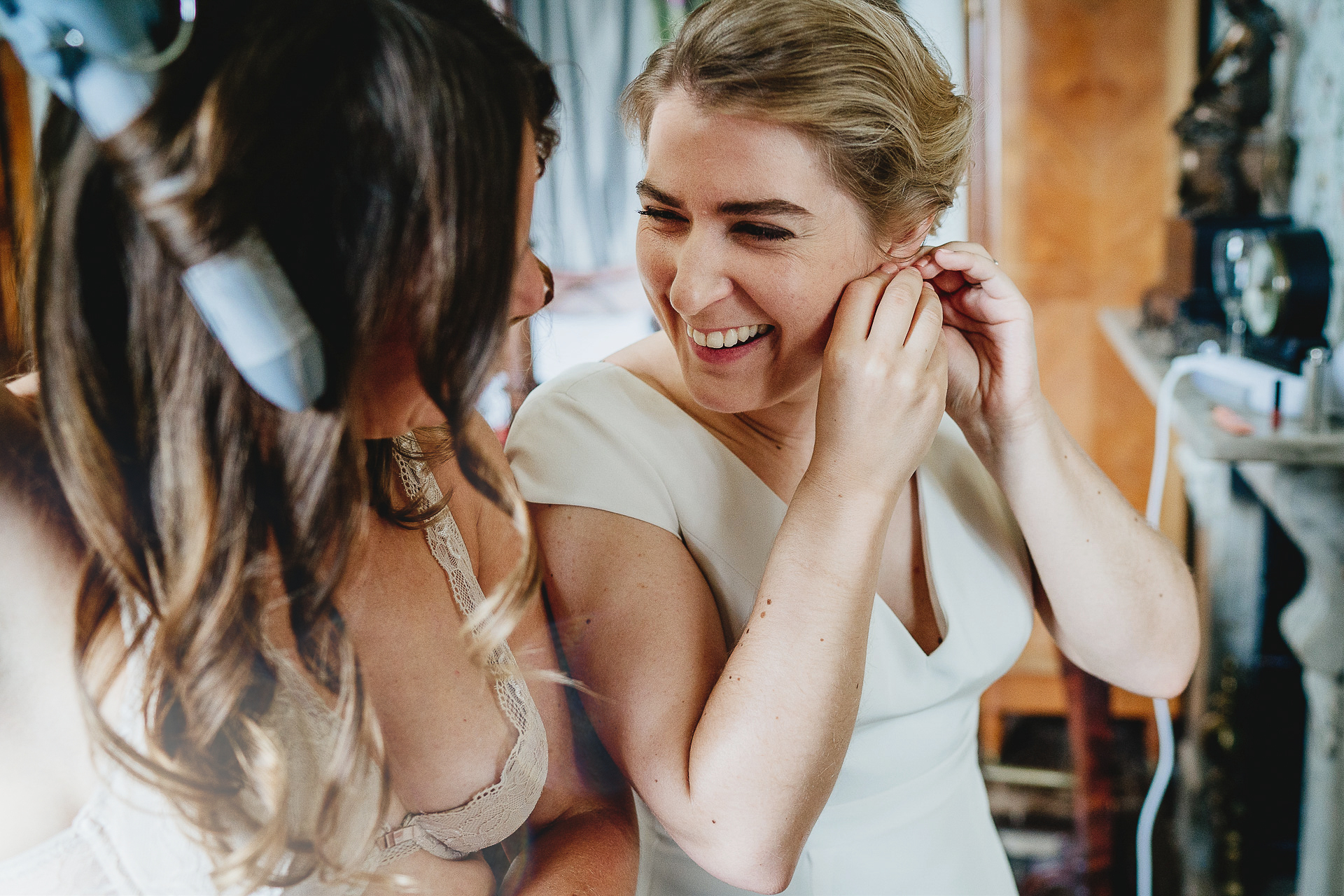 Bride smiling joyfully while getting ready with bridesmaid