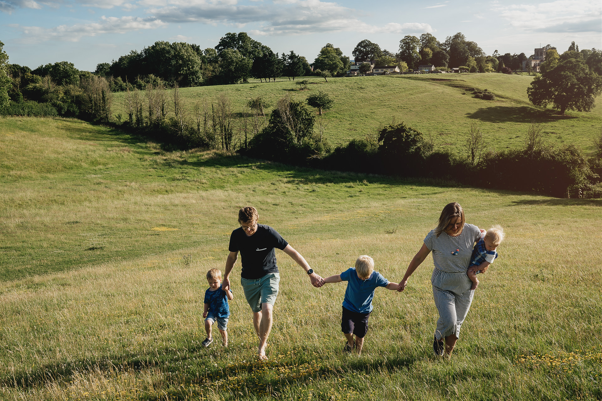 A family walking hand in hand in evening sunshine with a church on the hills behind them