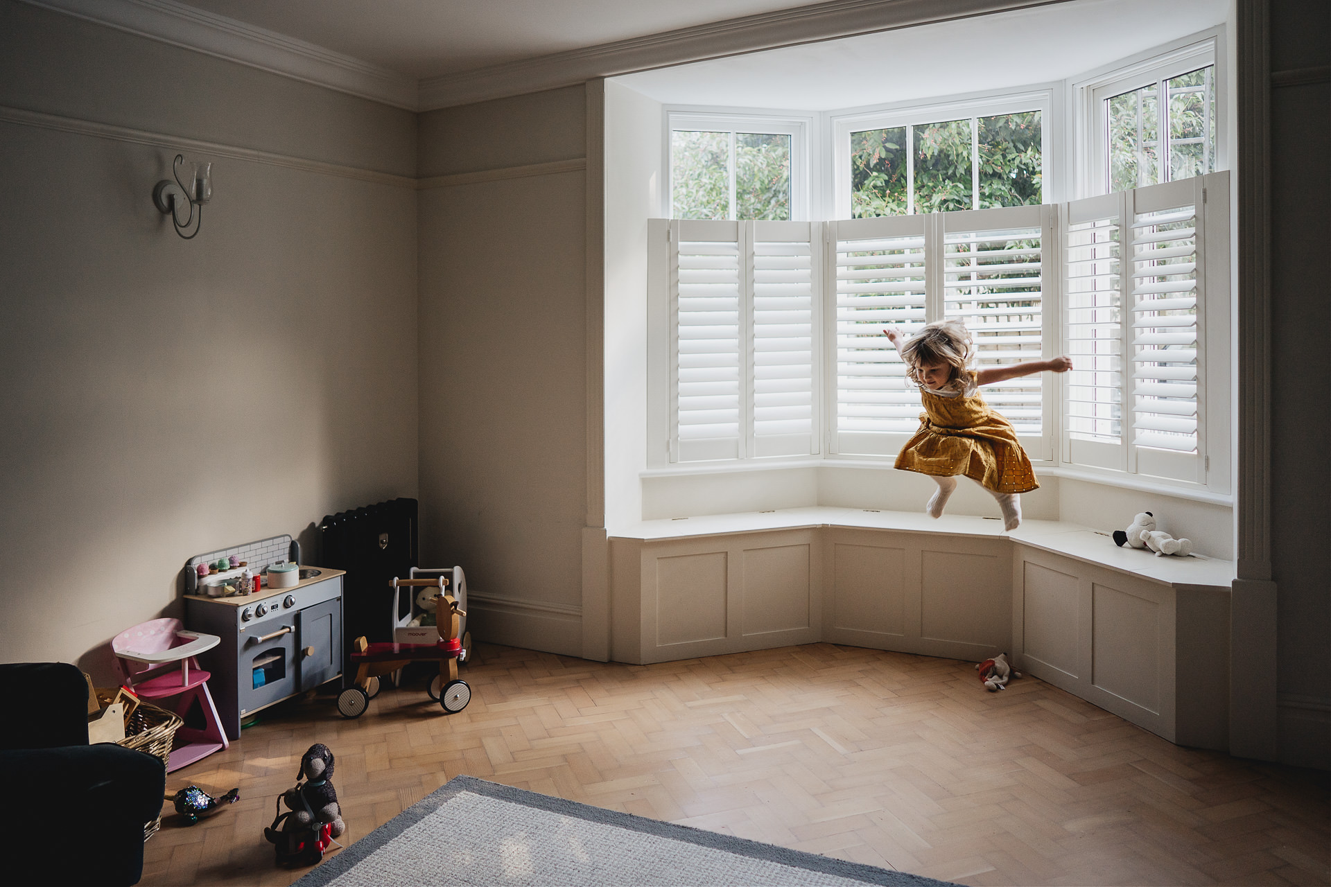 A young girl jumping off a window ledge in a living room
