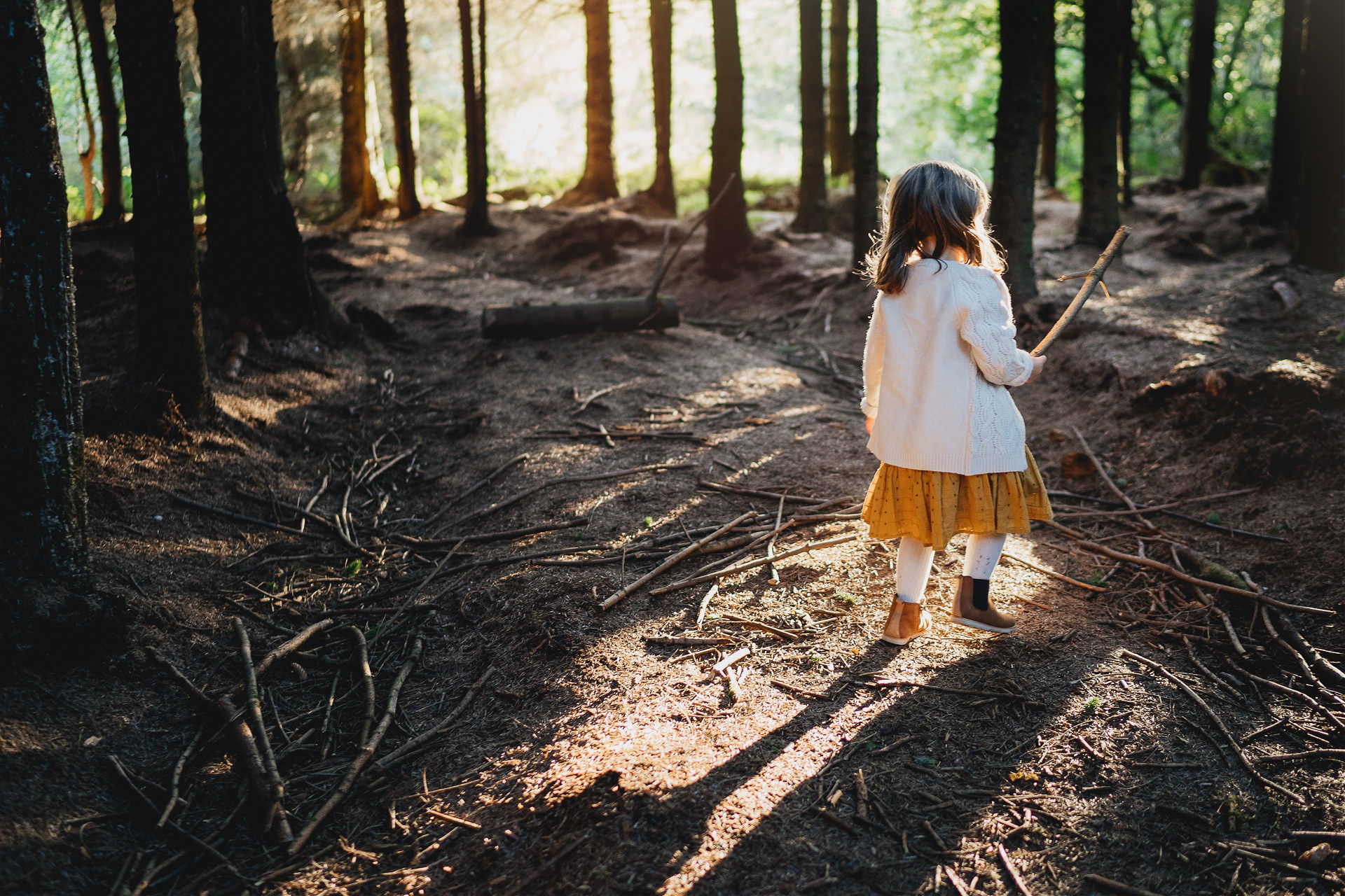 A young girl exploring woods with a stick in her hand