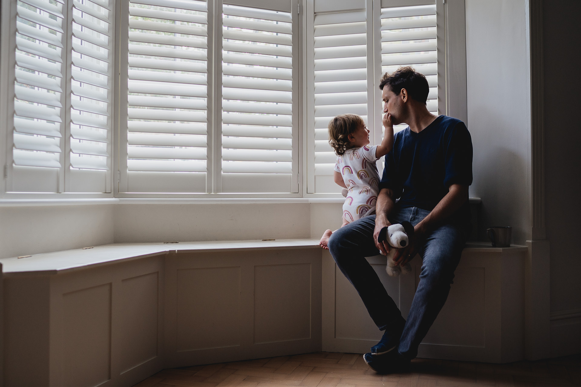 A father and daughter sitting on a window seat in front of shutters