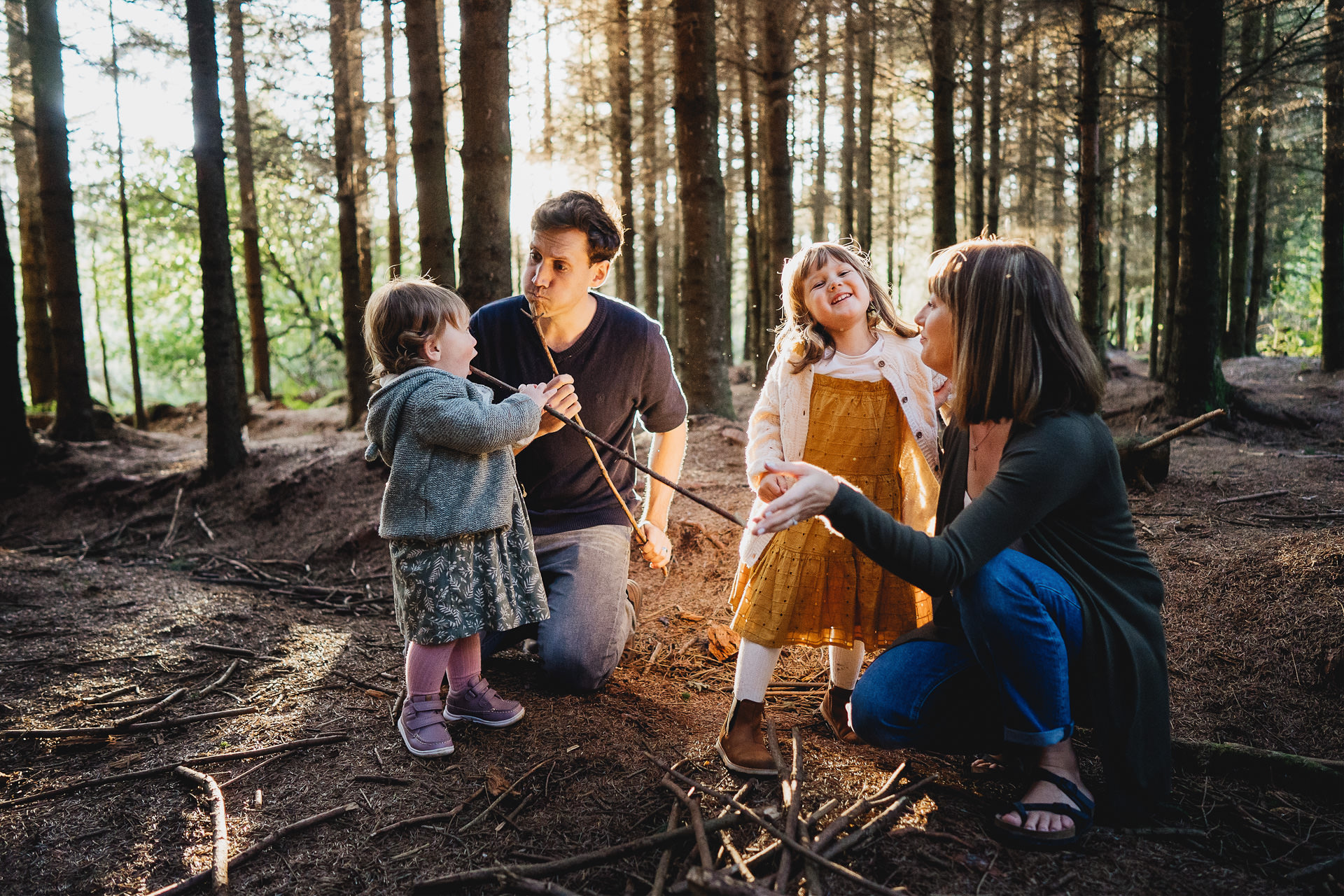 A family in the woods in evening light, with an imaginary campfire and sticks