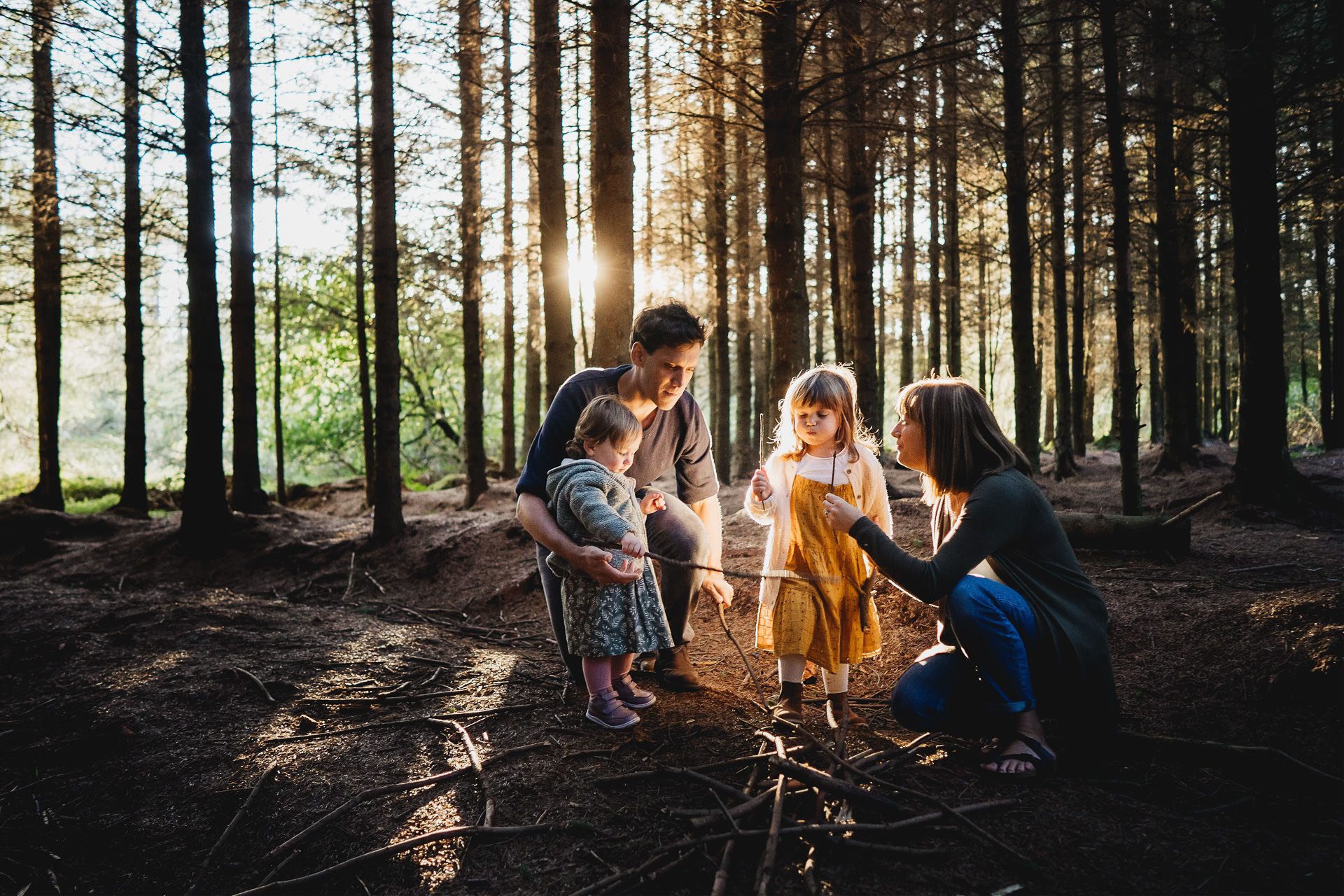 A family in the woods in evening light, with an imaginary campfire and sticks