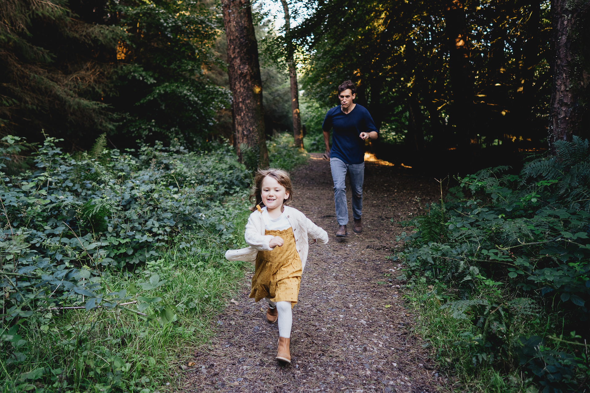 Father chasing his laughing daughter down a woodland pathway