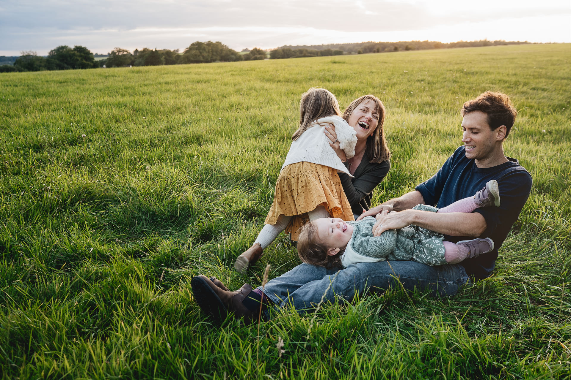 Two parents and children laughing and cuddling in a field