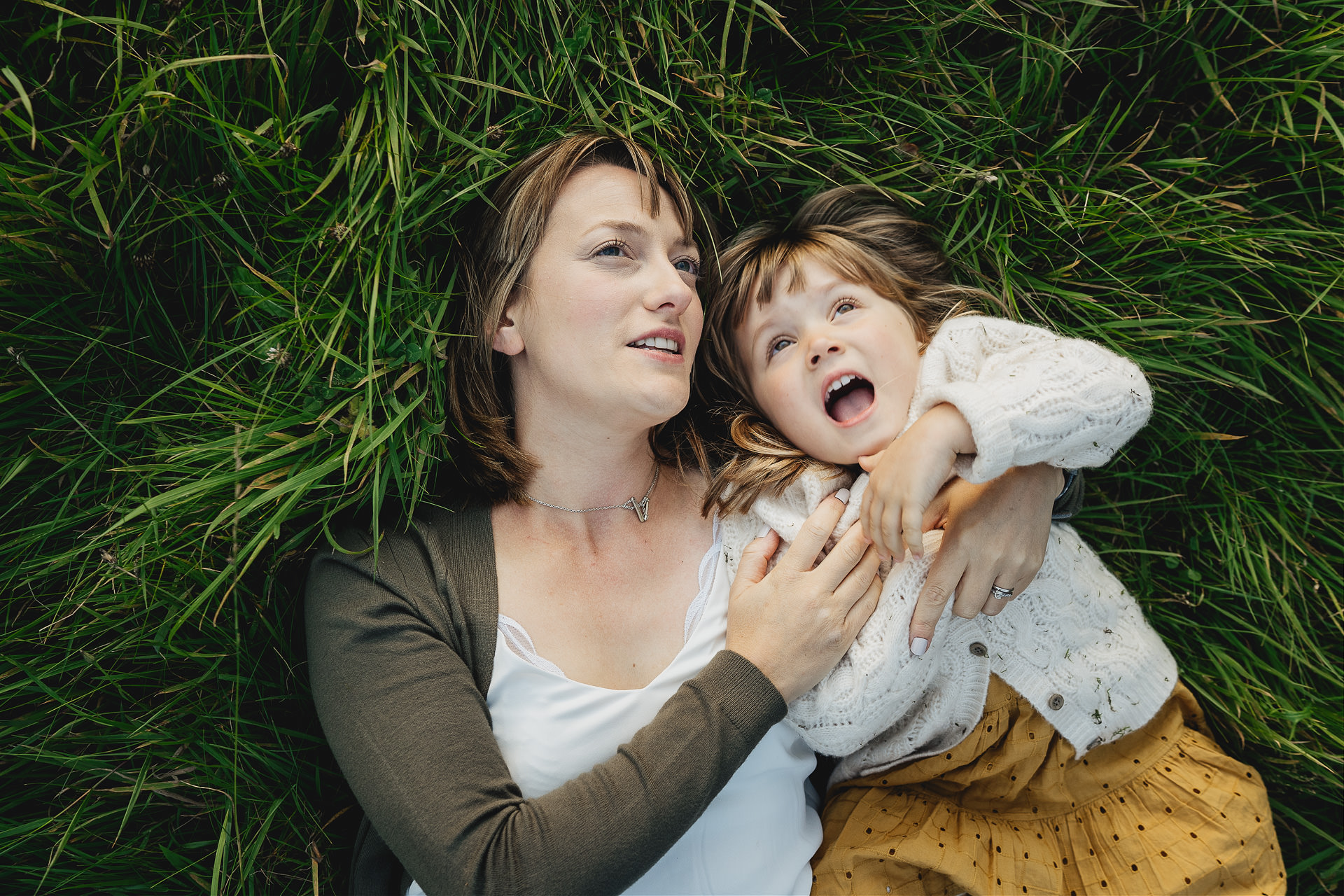 Mother and daughter lying in the grass together looking up at the sky