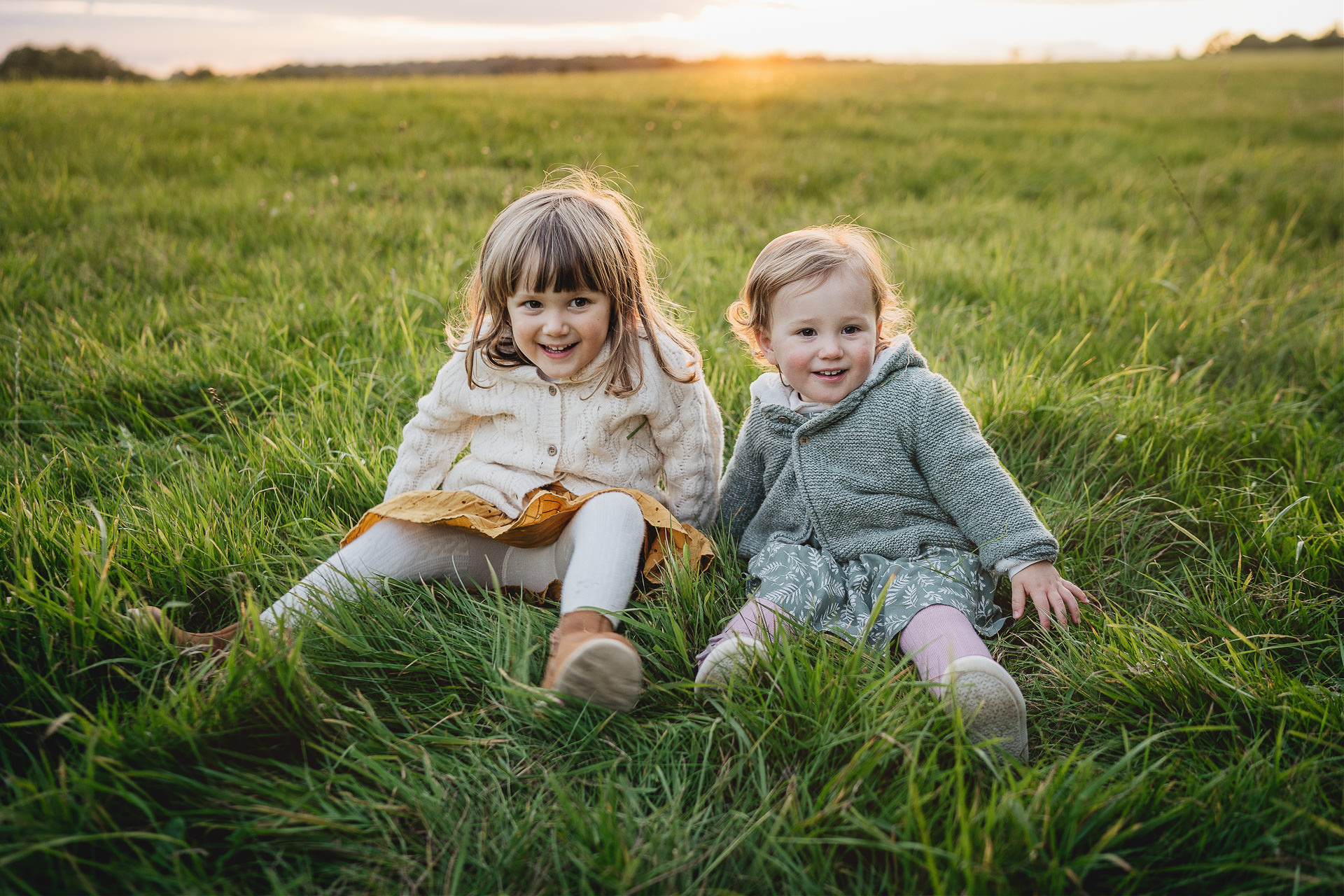 Two young sisters sitting in a field together with sunset behind