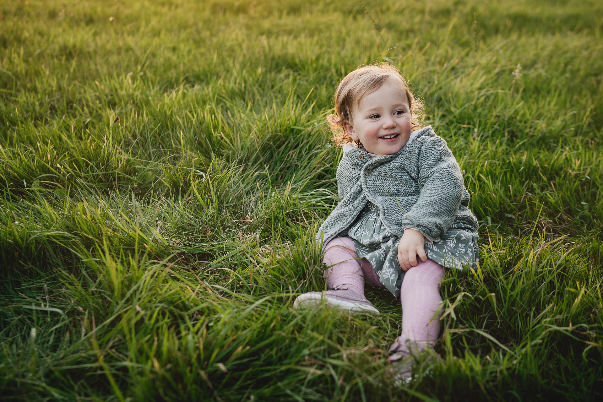 A toddler girl smiling in a field at sunset