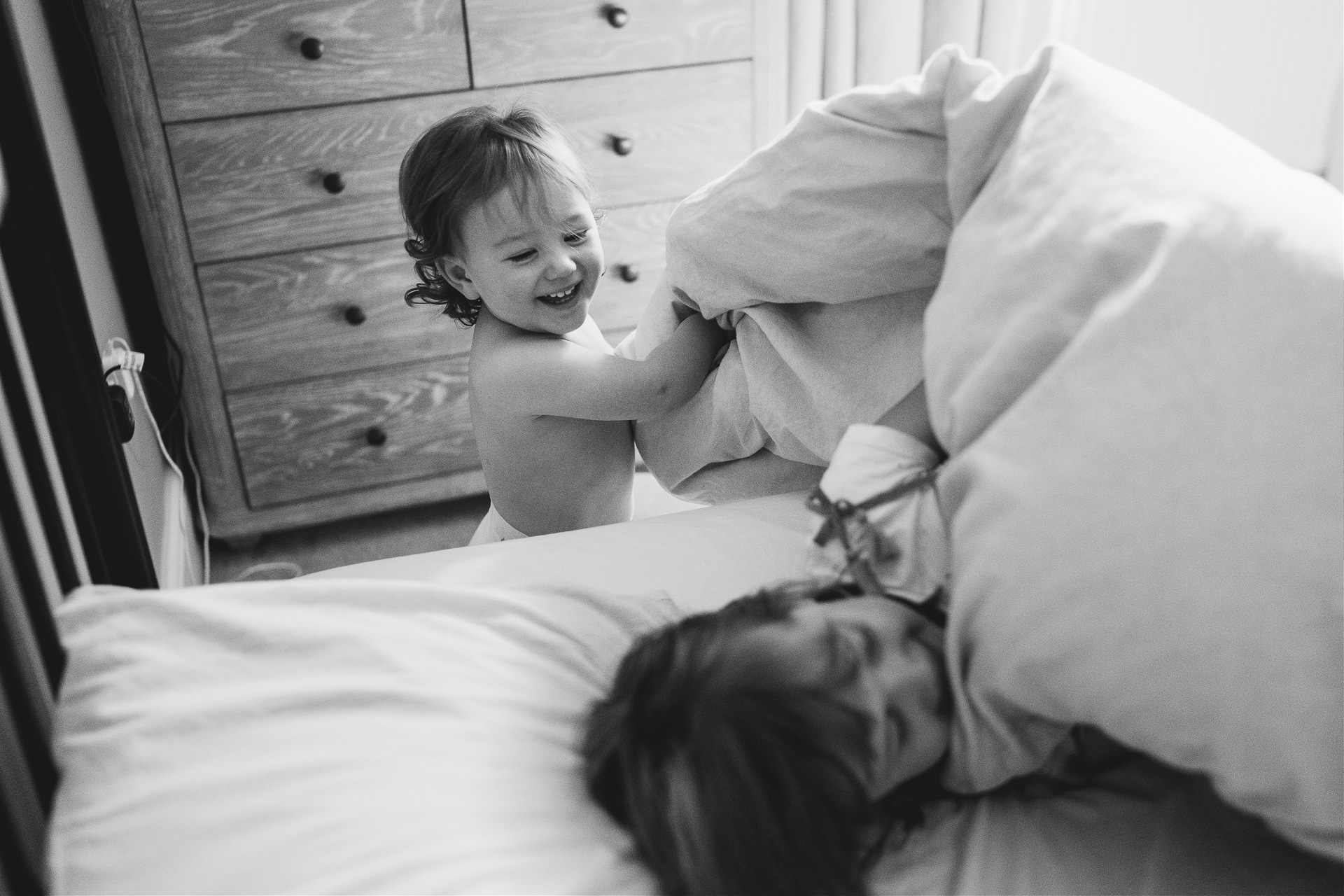 A toddler laughing as she pulls back the duvet cover on her sister