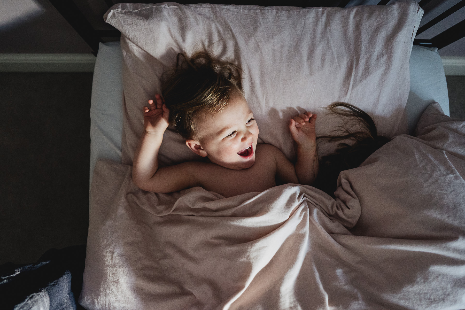 A young girl laughing in a bed with pink bedding
