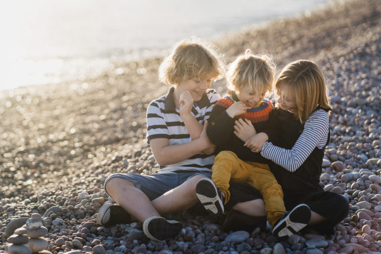 Three siblings laughing together on a pebble beach