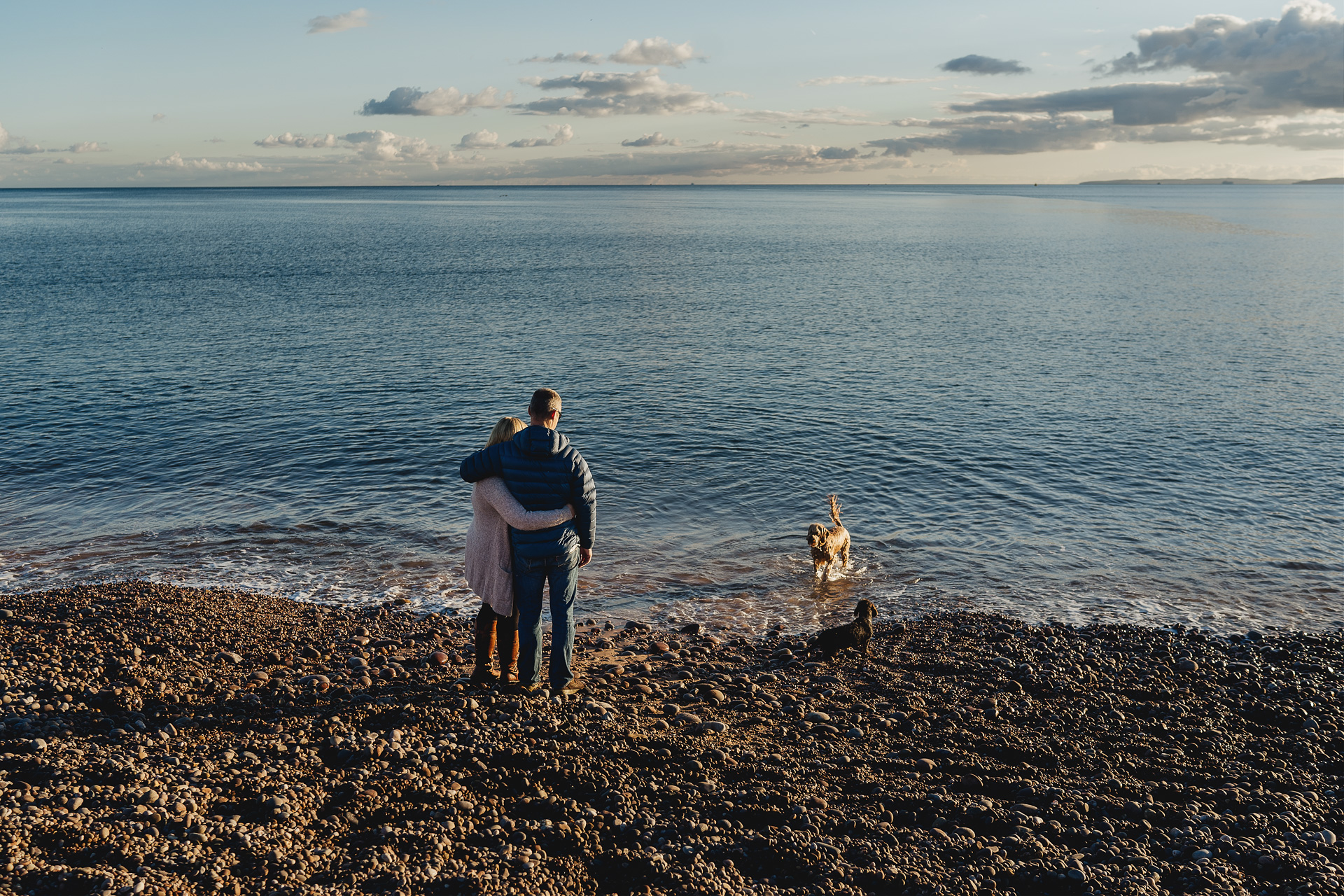 A man and woman with arms around each other looking at the sea