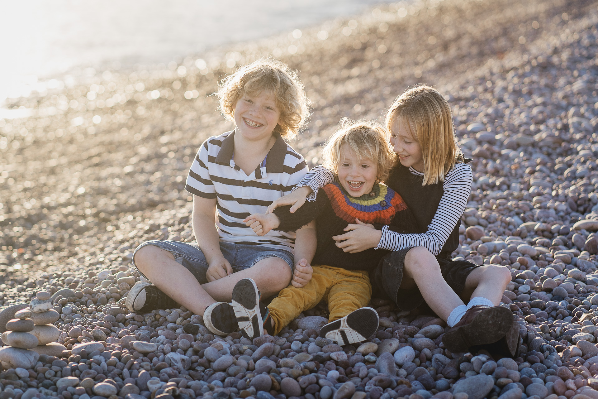 Three children laughing together on a pebble beach