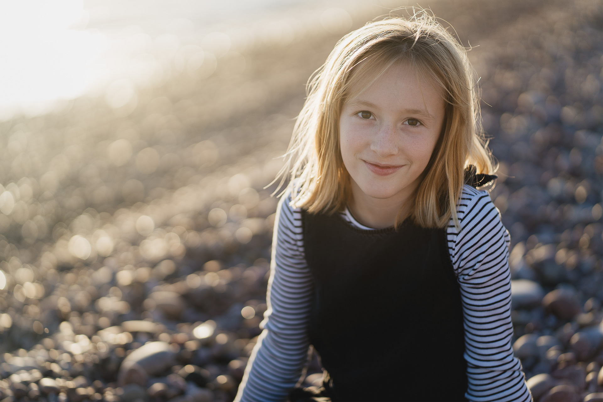 A young girl sitting on the beach smiling at the camera