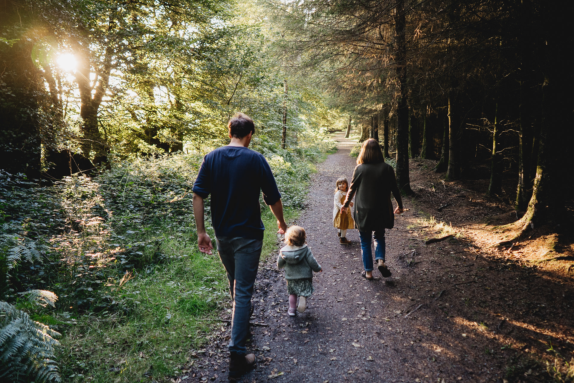 Best Devon family photography of two parents with two young children walking along a woodland path