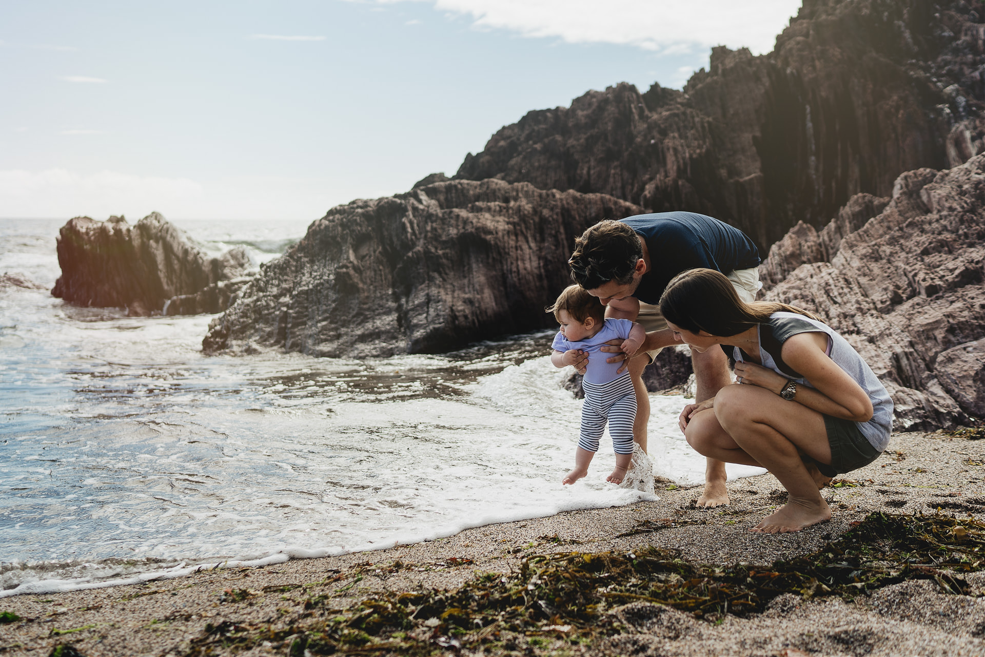Devon family photography at the beach of two parents with their baby daughter paddling at the sea