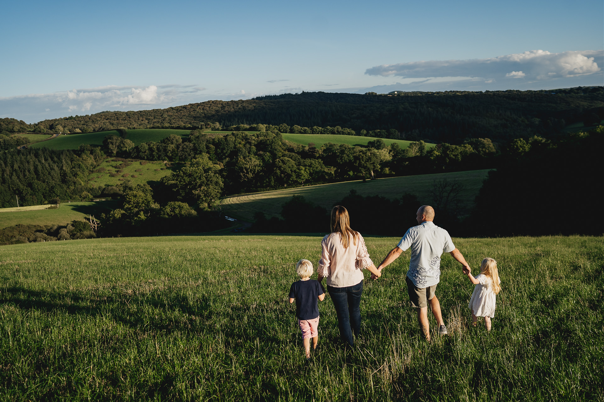 Family photography of two parents and two children holding hands and looking across Devon hills