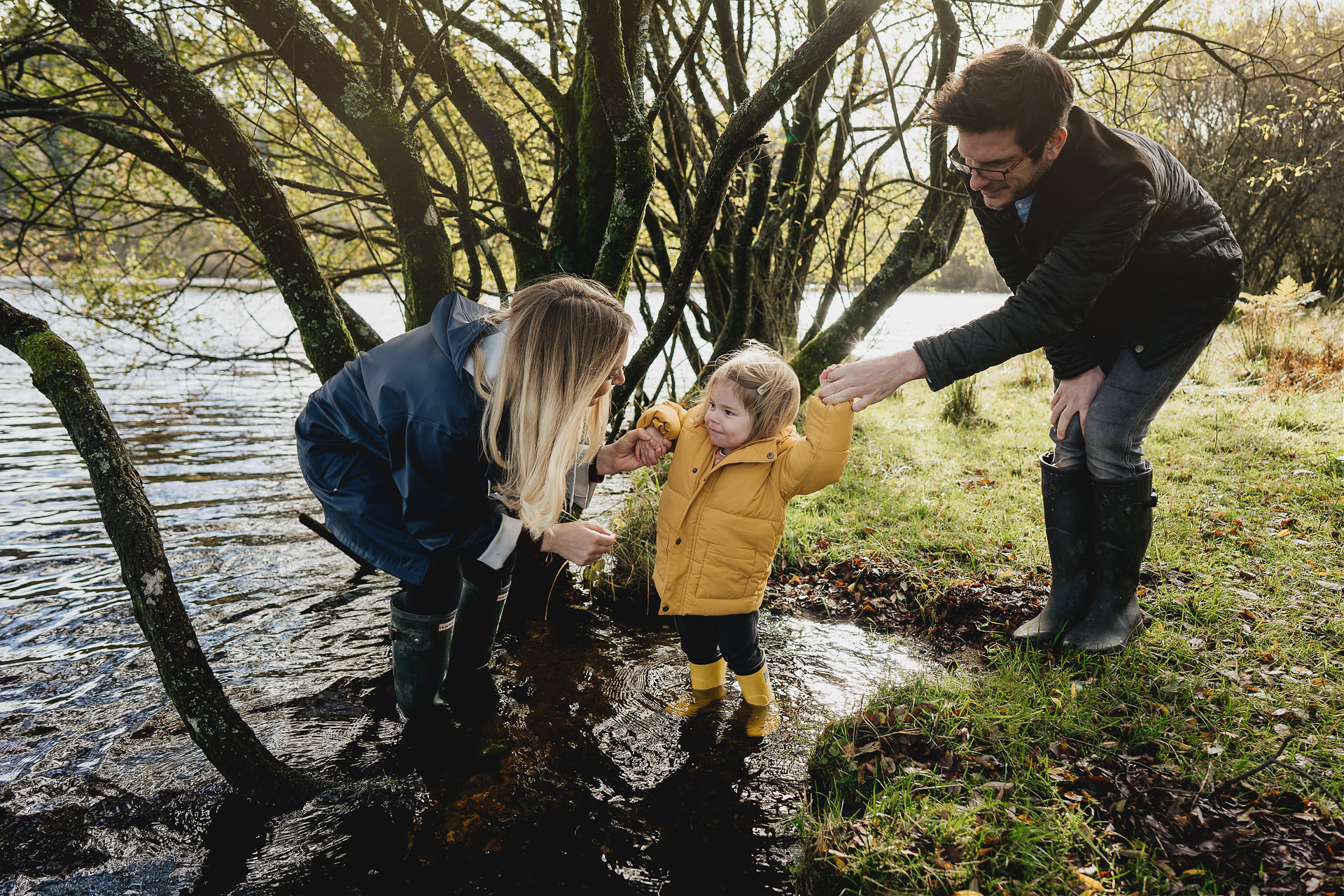 A family photography session on Dartmoor with a young girl in a yellow raincoat splashing in some water with her parents