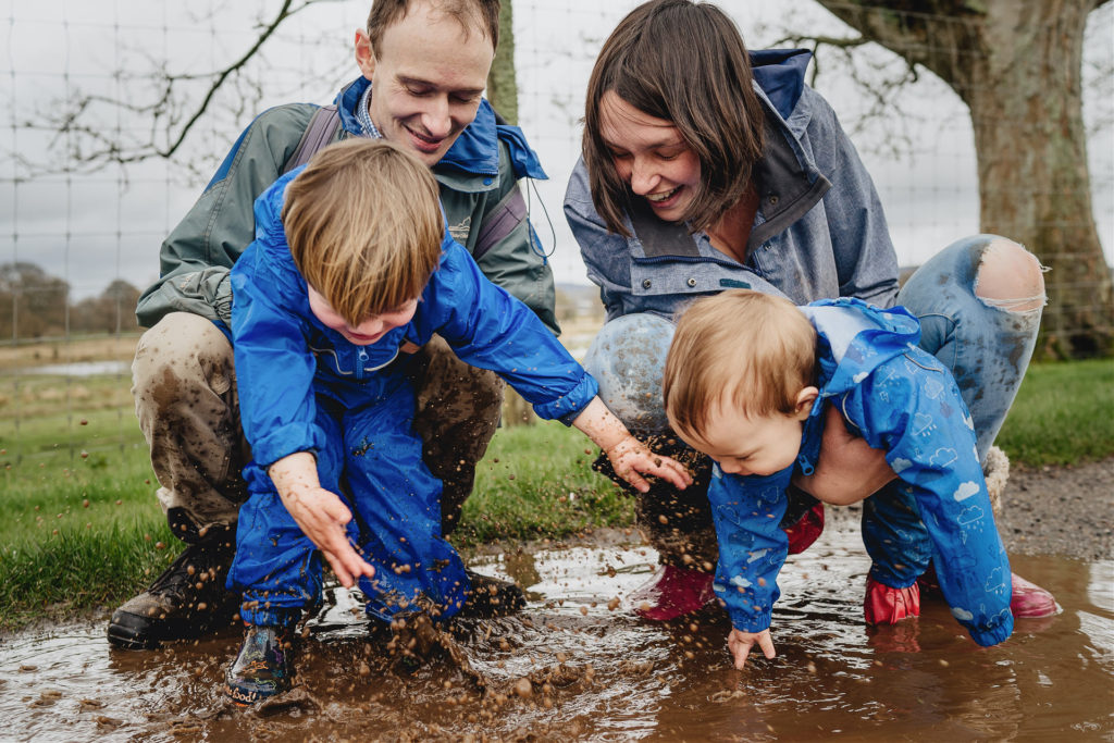 A family with young children splashing in a puddle