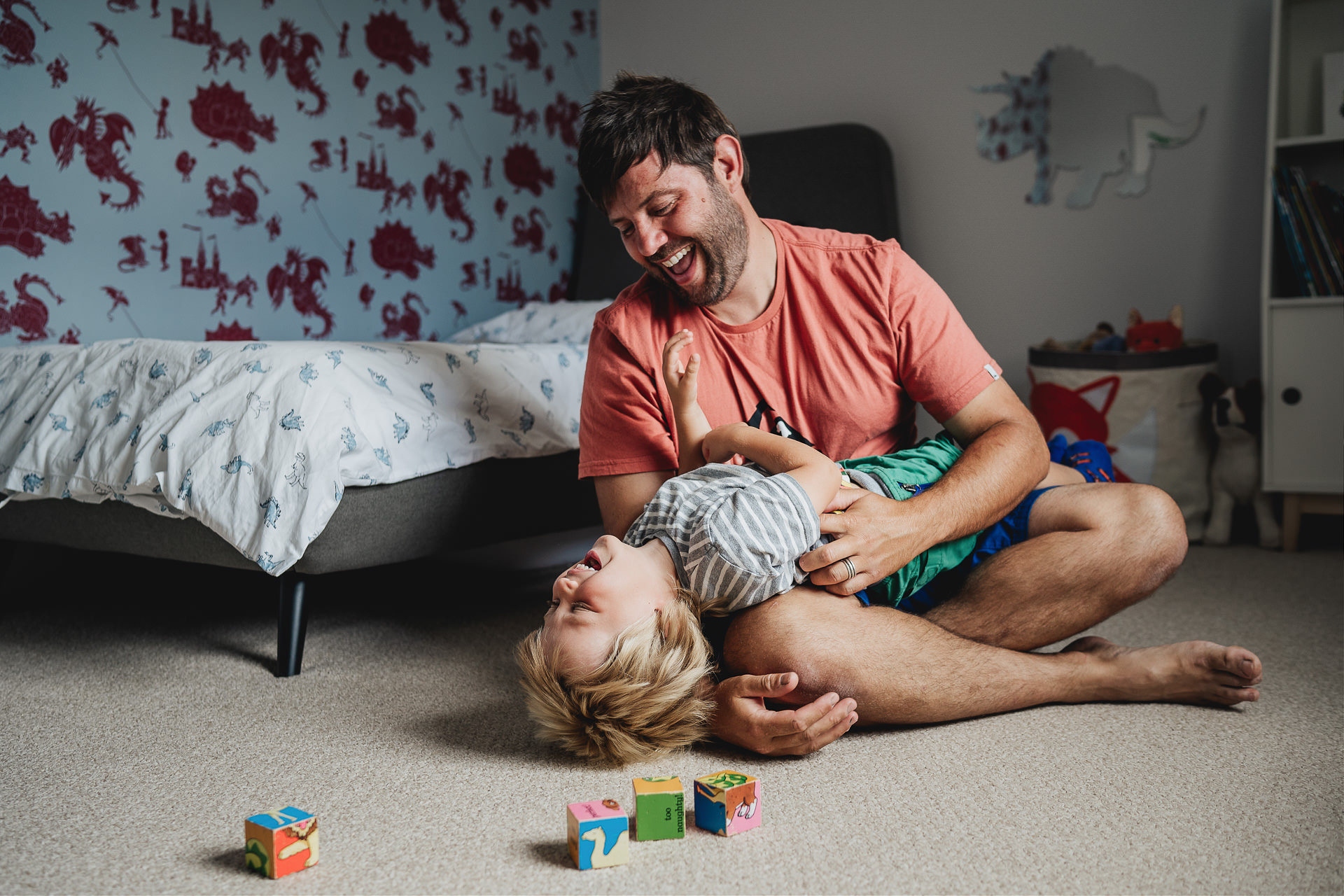 Best Devon family photography at home of a father playing and laughing with young son in a bedroom