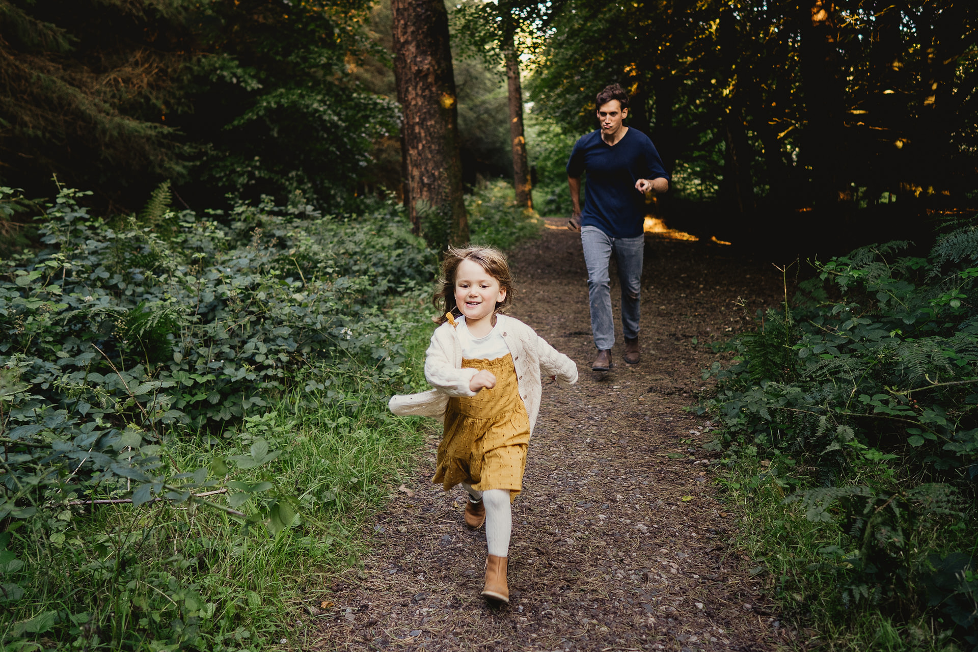 A father running with young daughter on a woodland path
