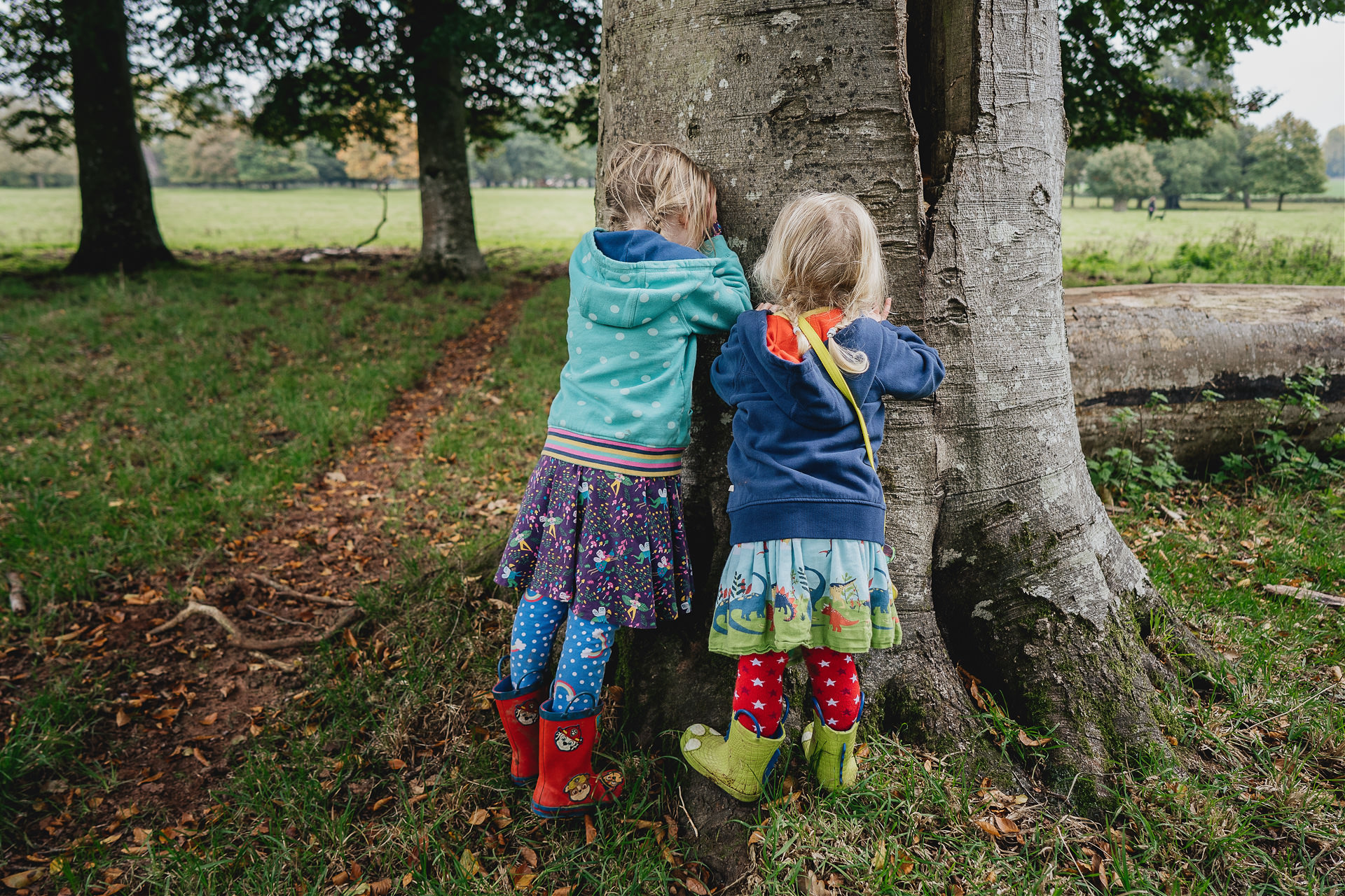 Two young girls playing hide and seek by a tree