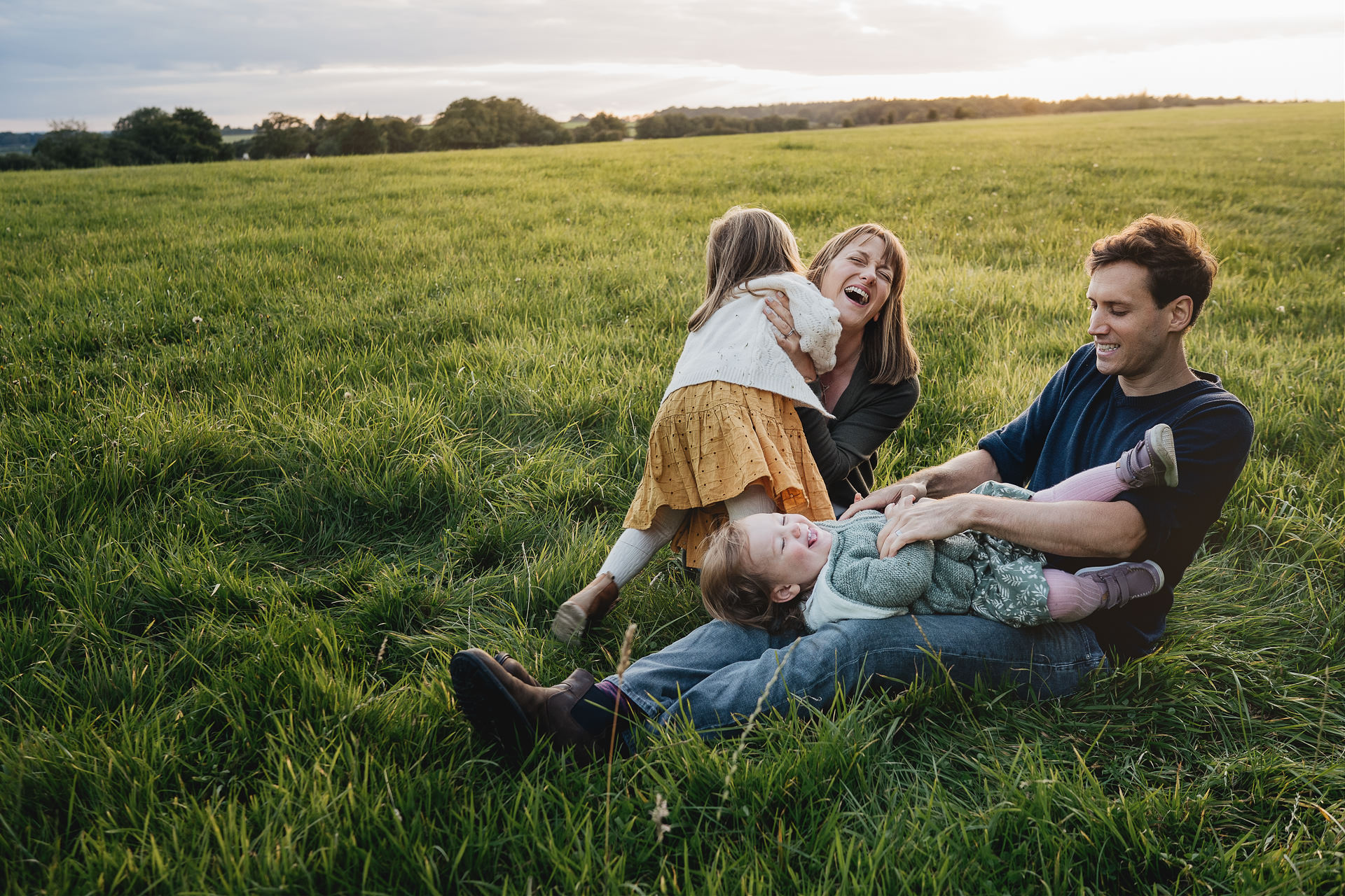 A relaxed family photography portrait of a family cuddling and laughing together in a field