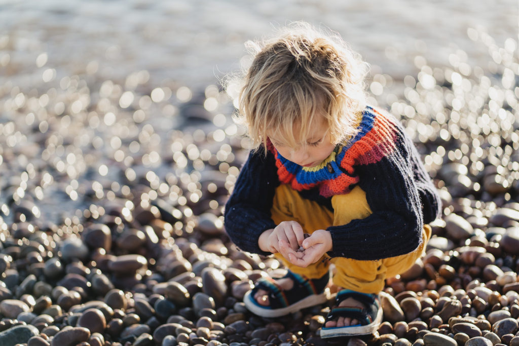 A young boy picking up pebbles on a beach in sunshine