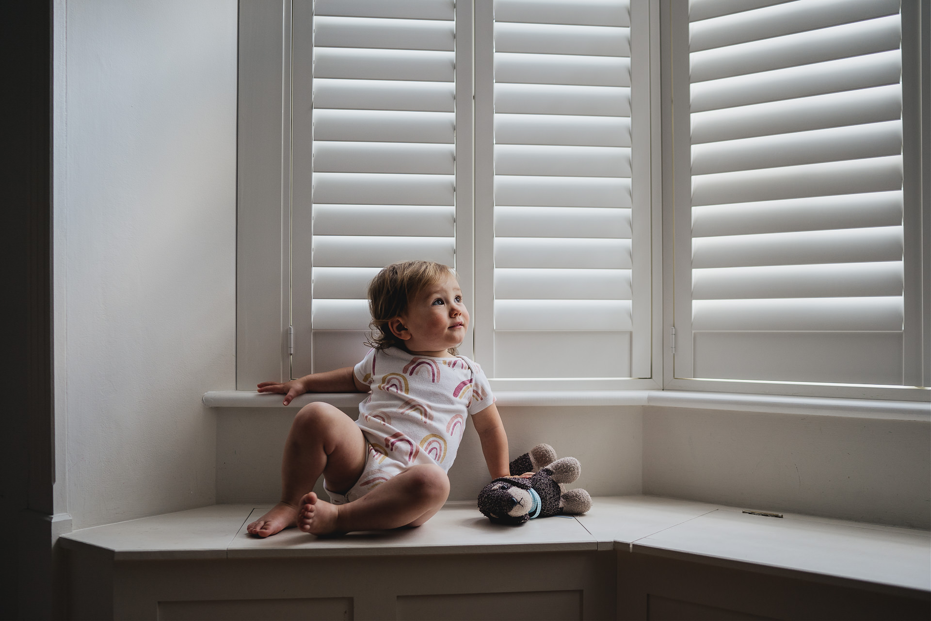 Best Devon family photography: a toddler sitting on a window ledge with a toy