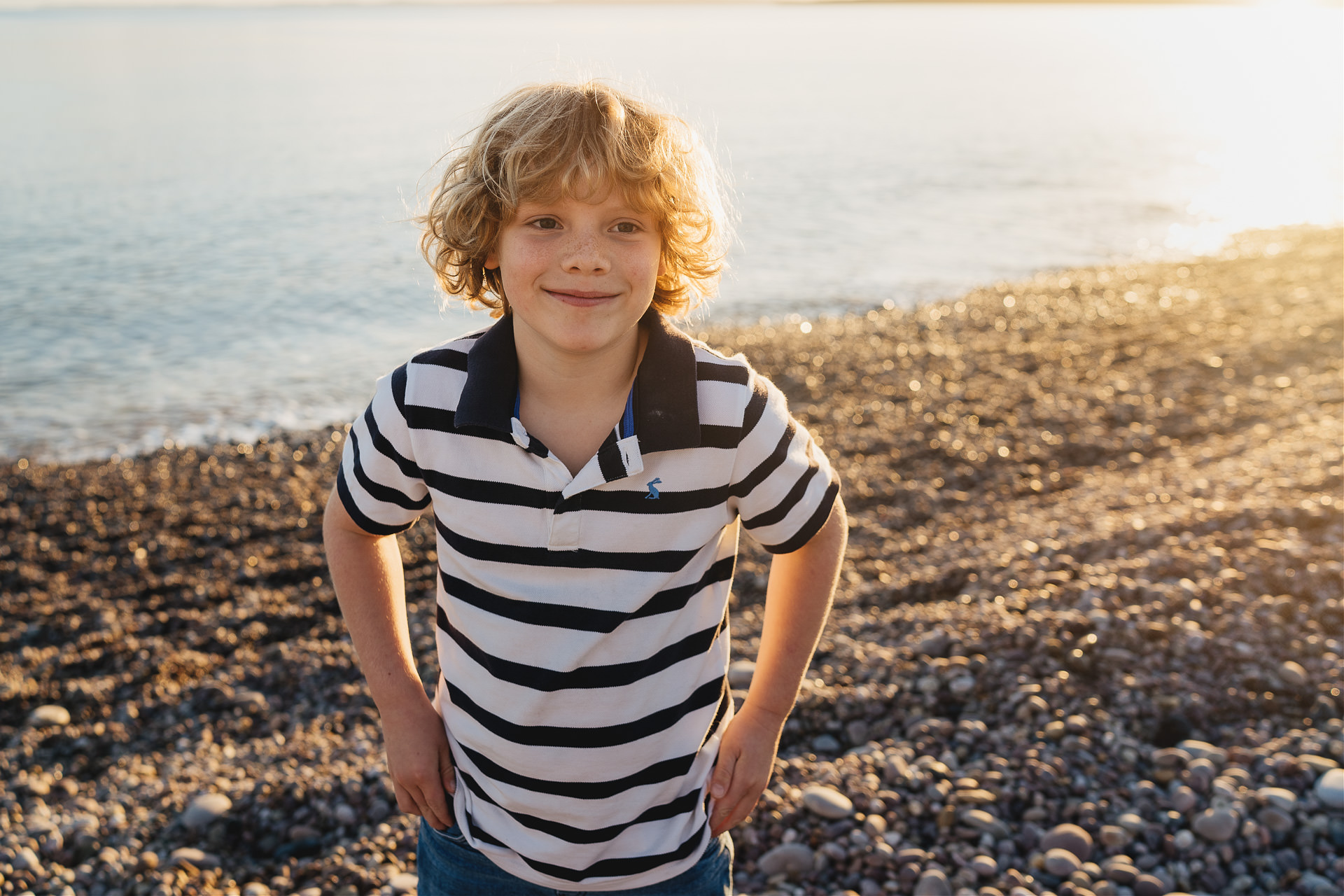 A boy smiling on the beach with sun setting behind
