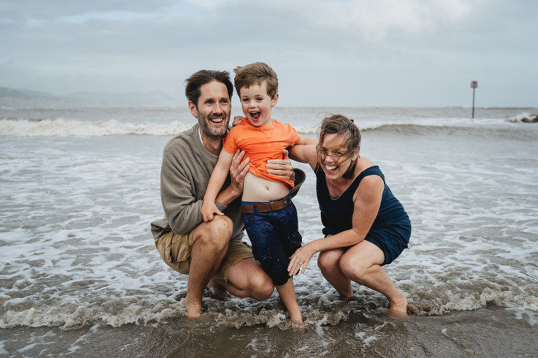 A family photography session at the beach, with parents and child laughing together in the sea