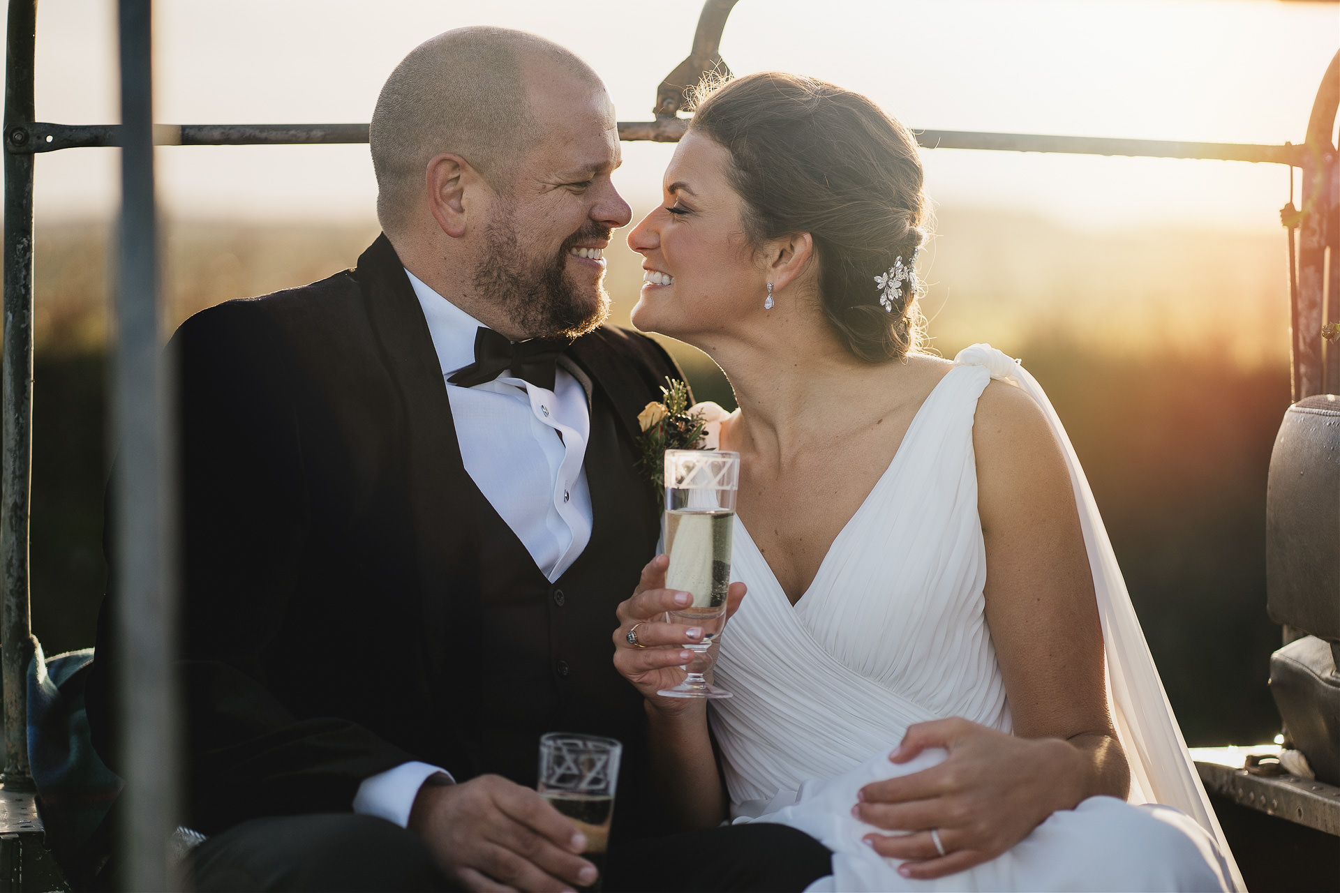 Bride and groom smiling at each other with sunset behind