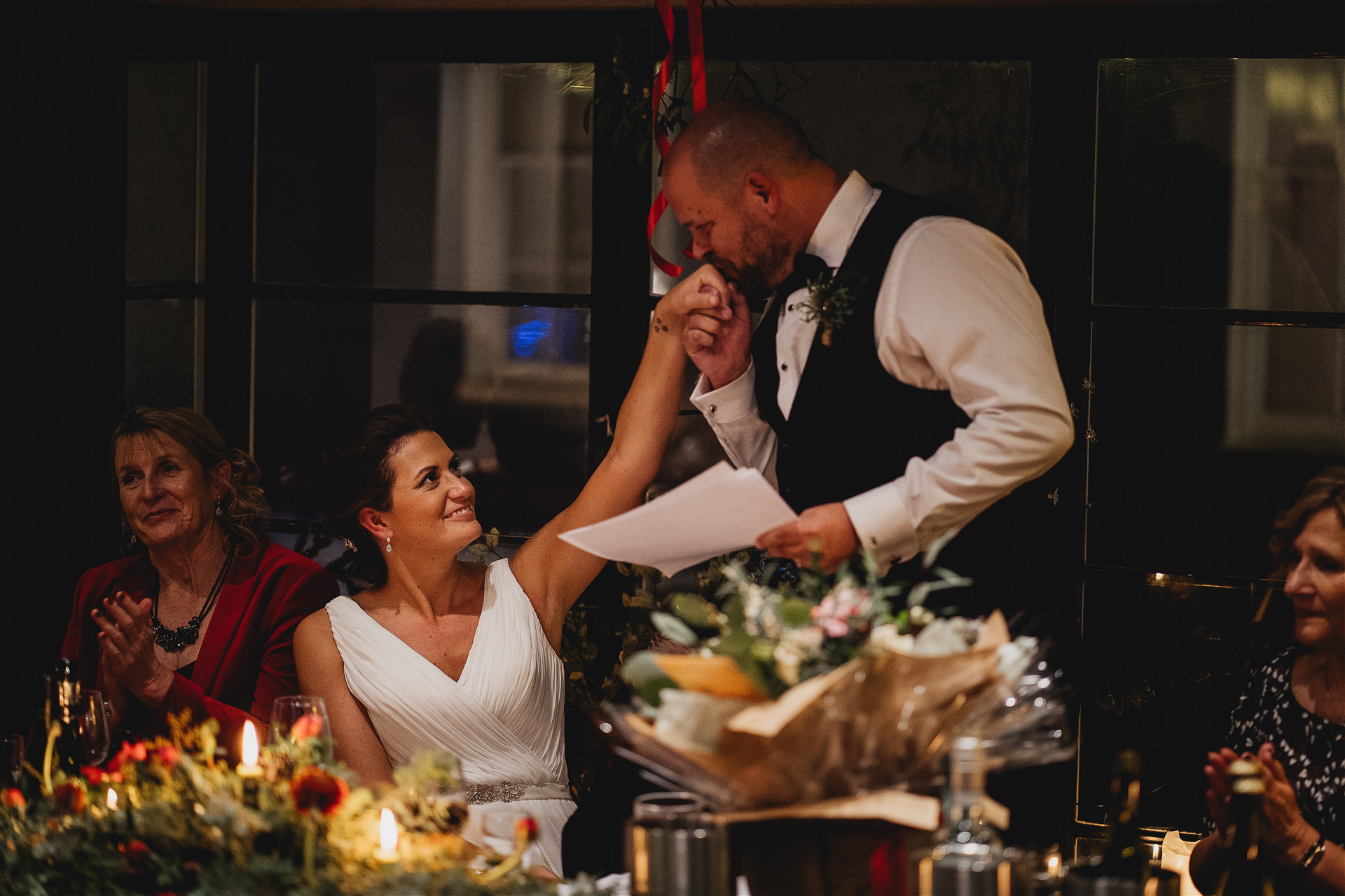 Groom kissing bride's hand at a dinner table