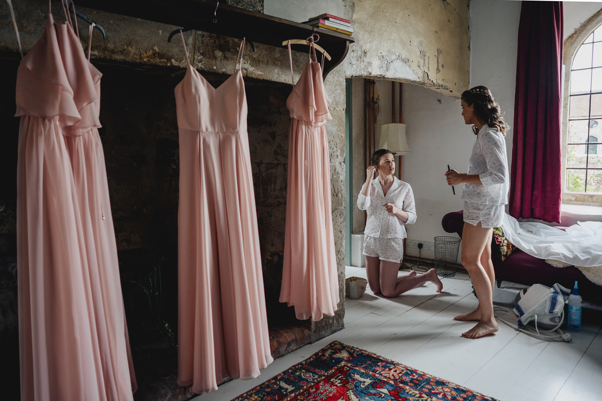 Bride talking to bridesmaid with pink dresses hanging up