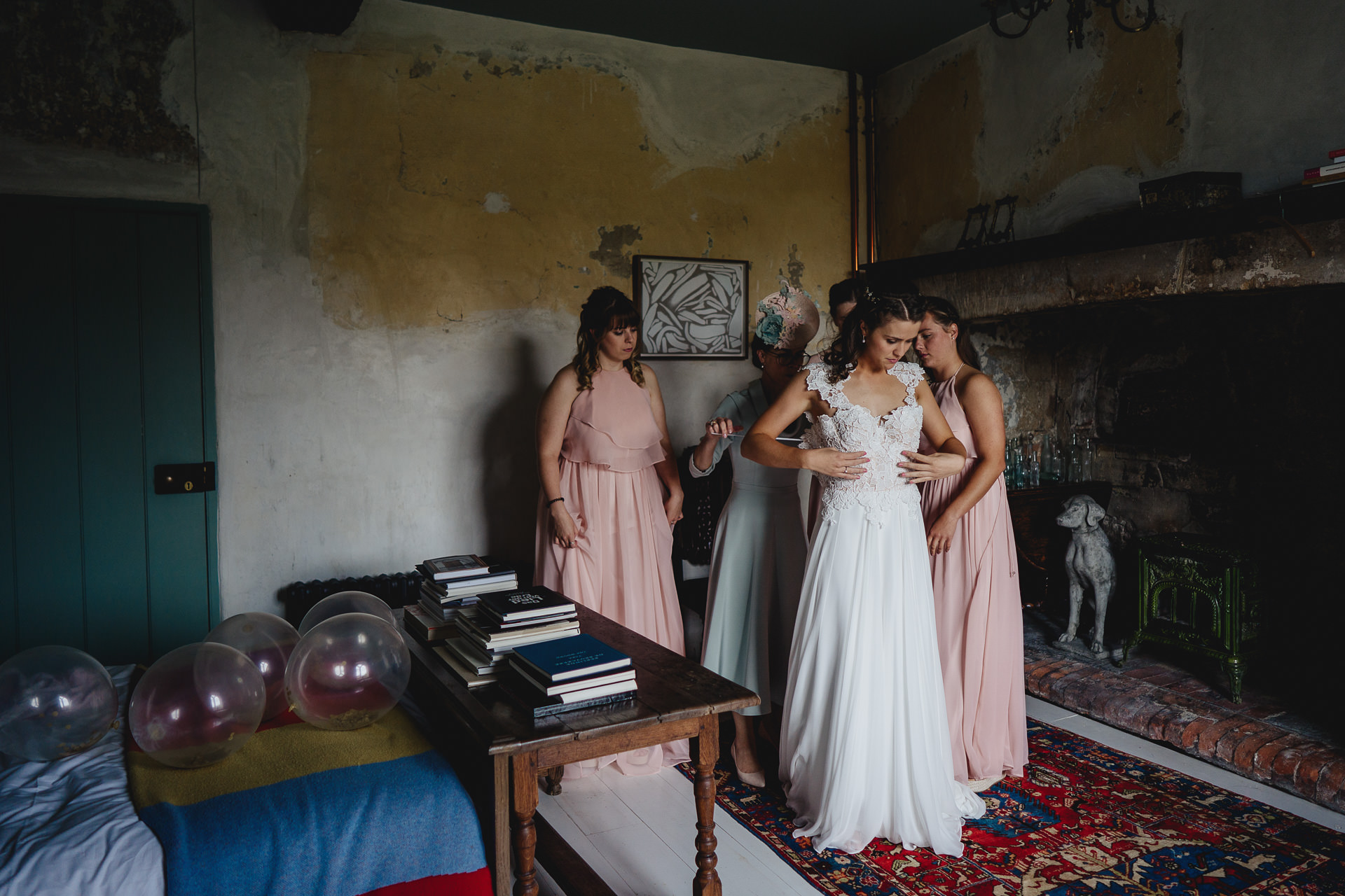 Bride with bridesmaids putting on wedding dress at Durslade Farmhouse