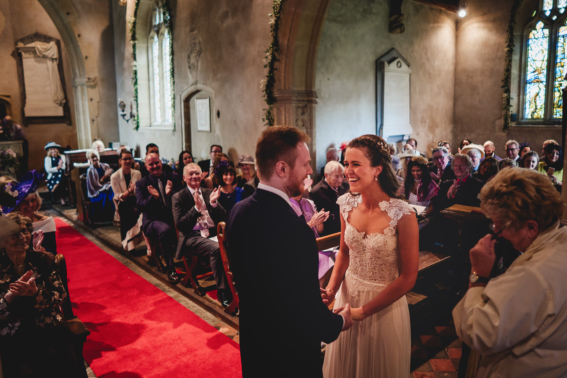 Bride and groom smiling at each other while guests applaud in church