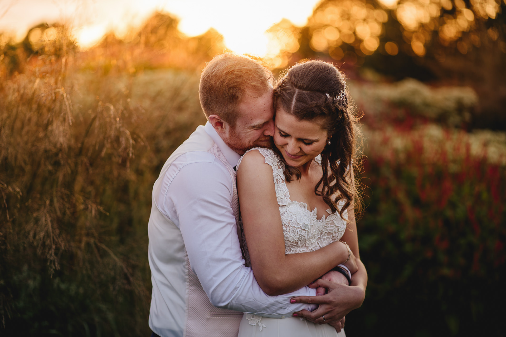 Bride and groom cuddling with golden sunset behind