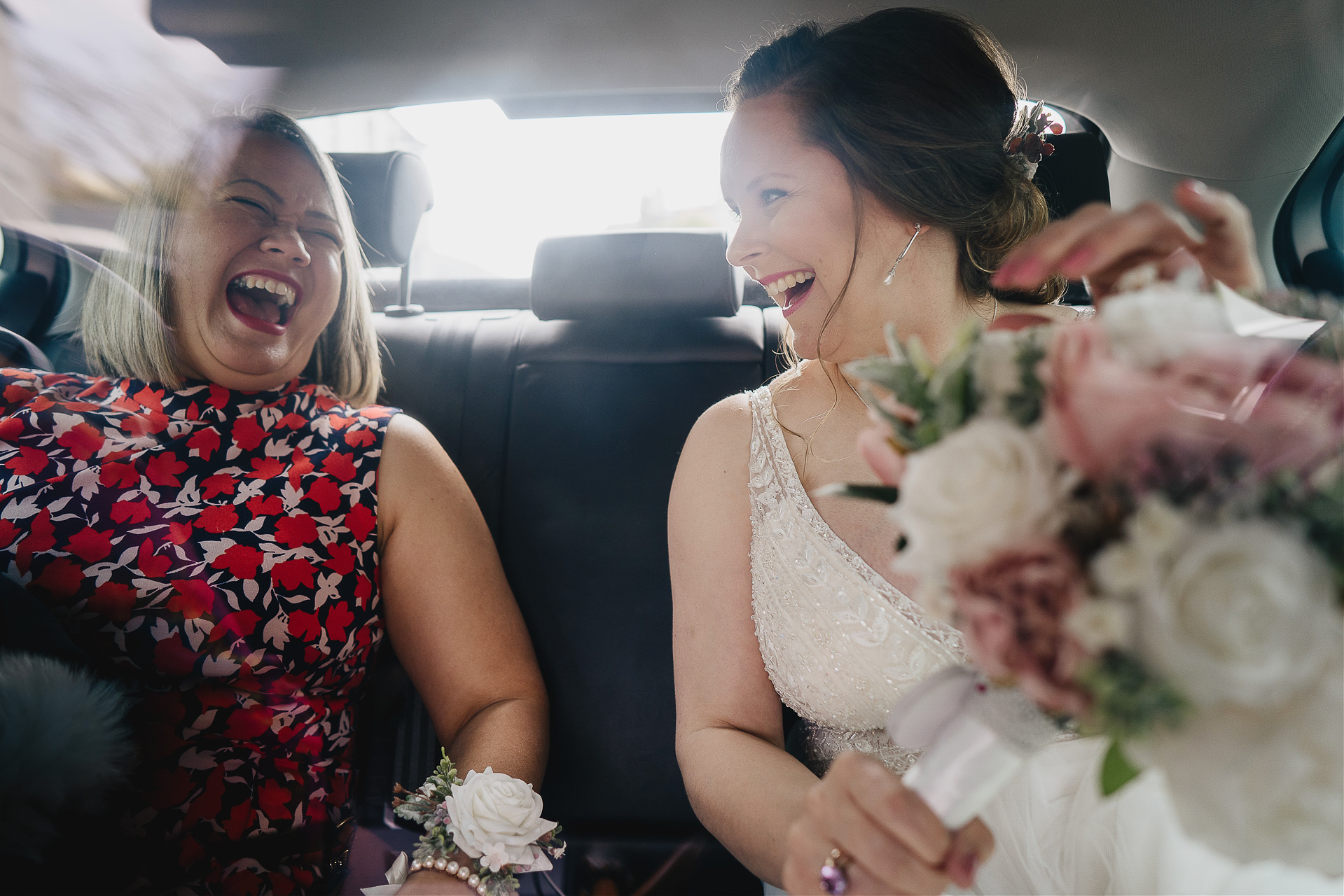 Bride and friend laughing together in taxi through plastic screen