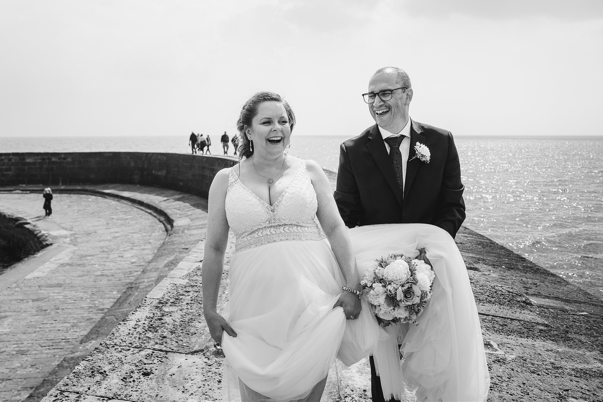 Bride and groom laughing together walking along the Lyme Regis Cobb