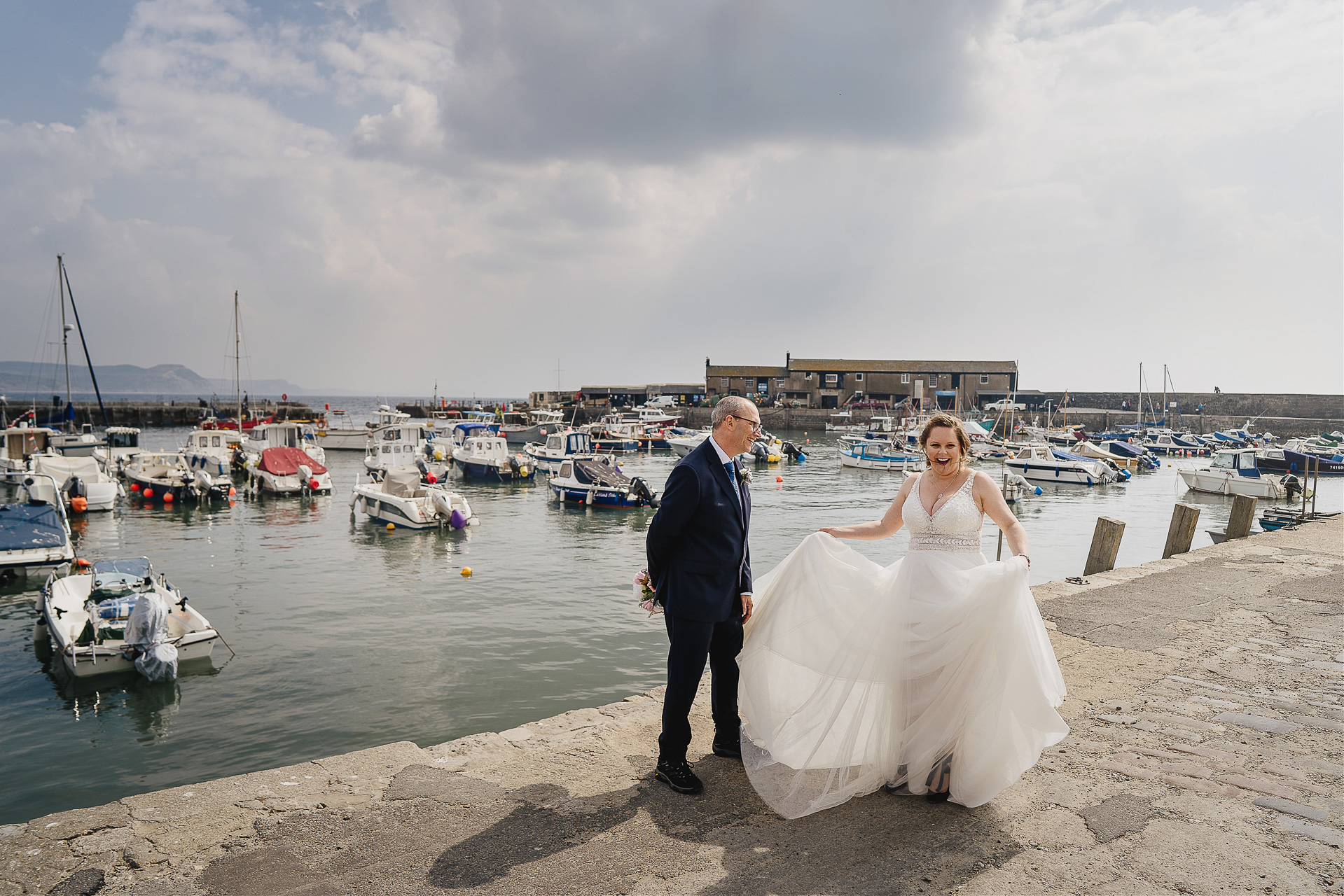 Elopement wedding by the sea, bride and groom laughing with boats in the harbour behind them
