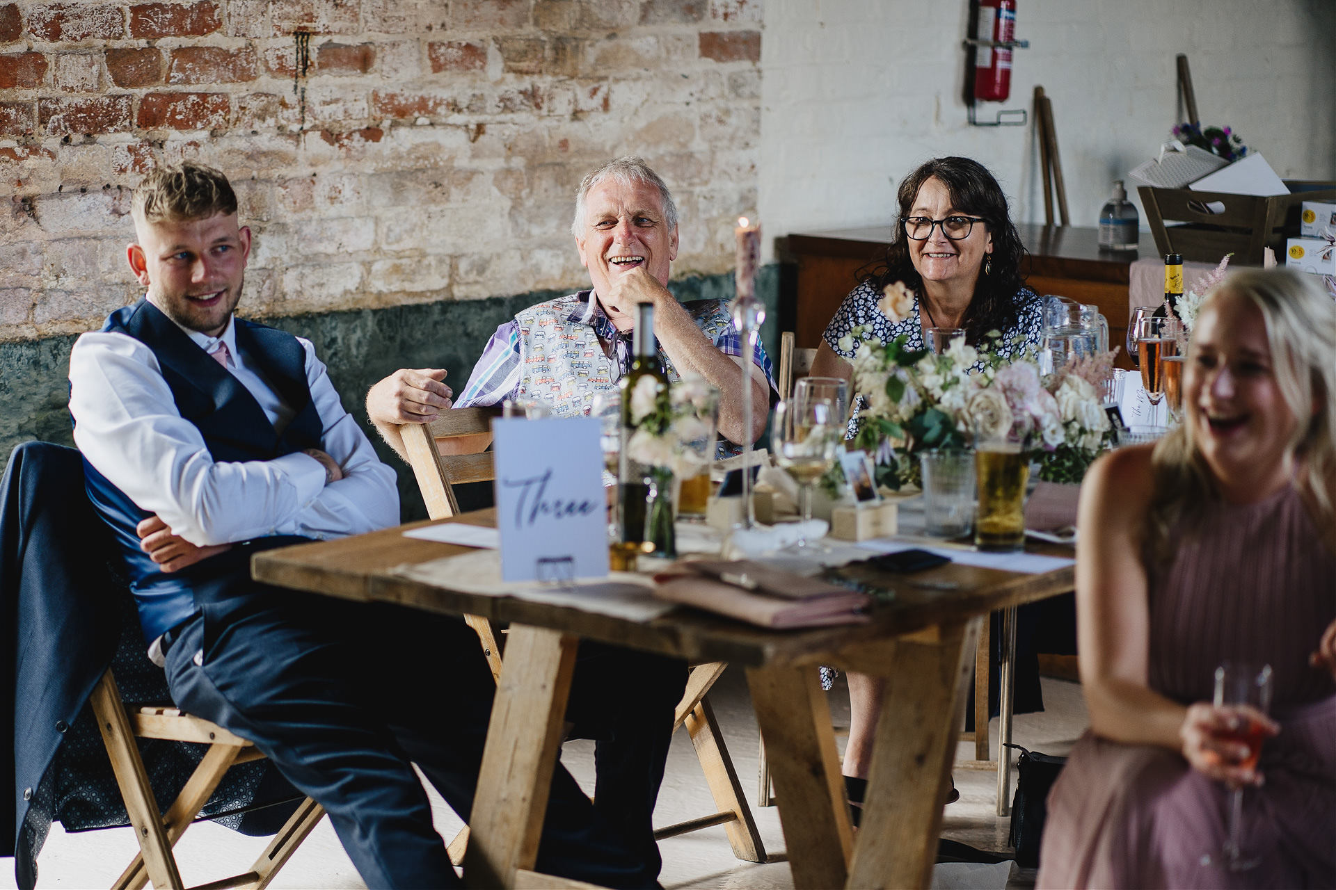 Wedding guests laughing during speeches in a rustic barn
