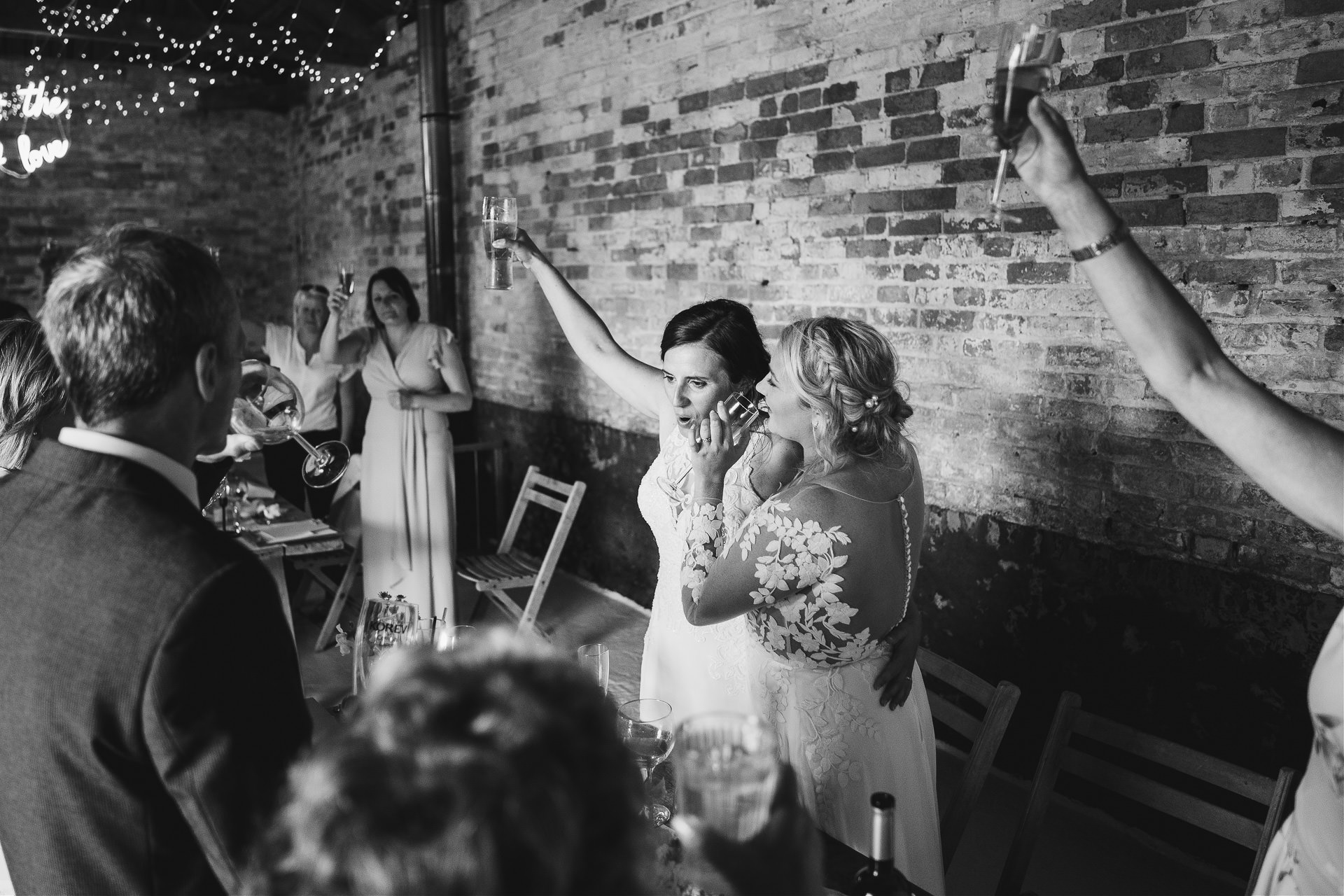 Two brides cuddling and raising glasses to their guests