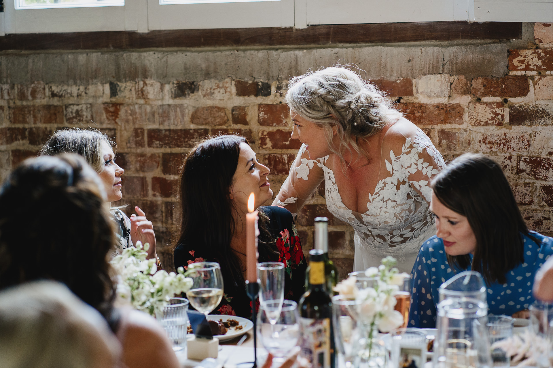 Bride and wedding guests laughing and chatting inside a rustic barn