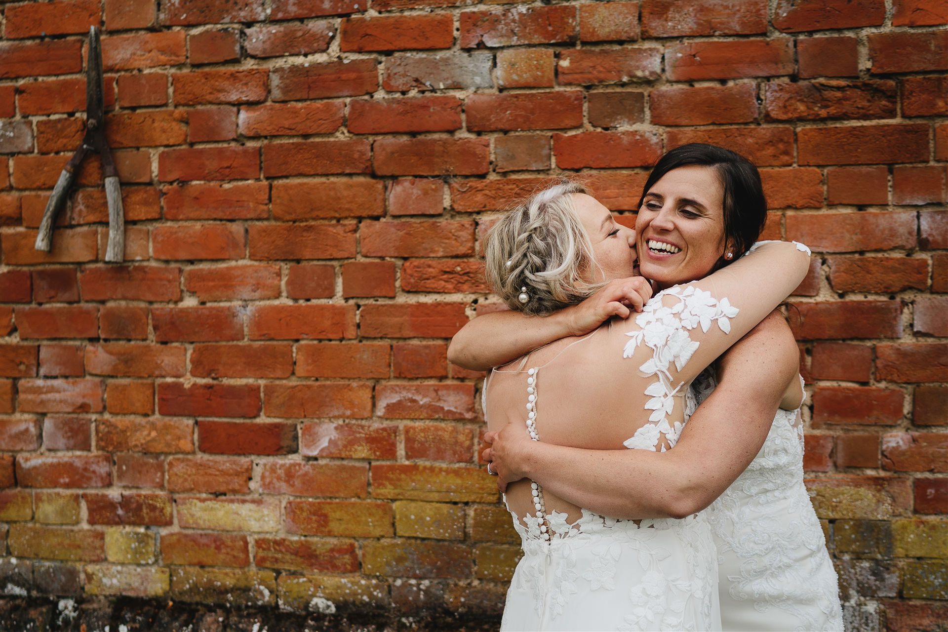 Two brides cuddling by an old wall at Cadhay in Devon