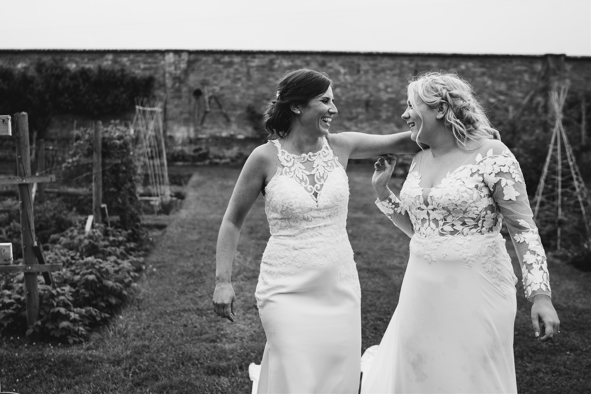 Bride and bride walking through allotments and smiling at each other 