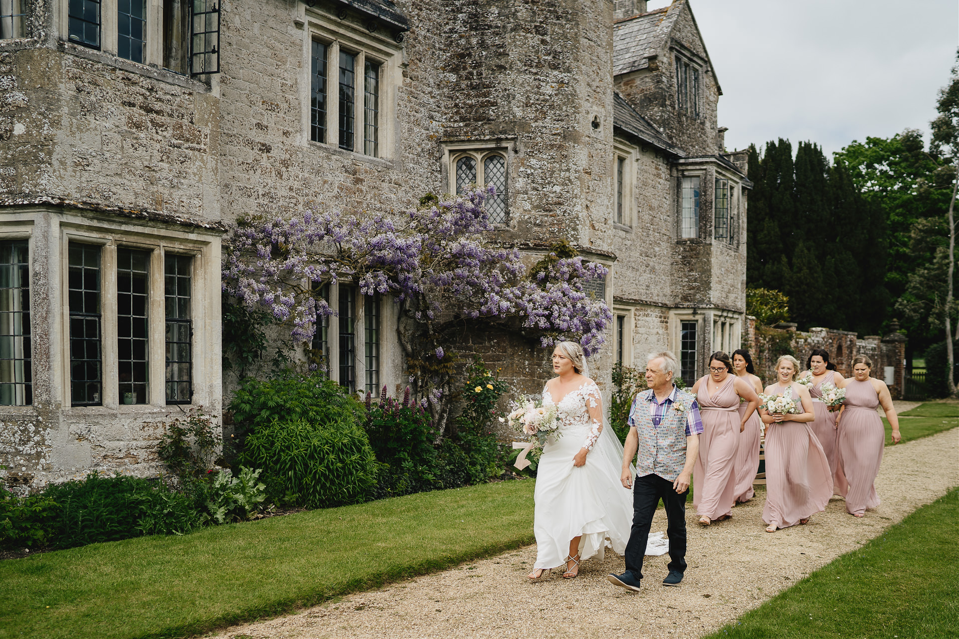 Bride walking past an Elizabethan house on the way to her Cadhay wedding ceremony