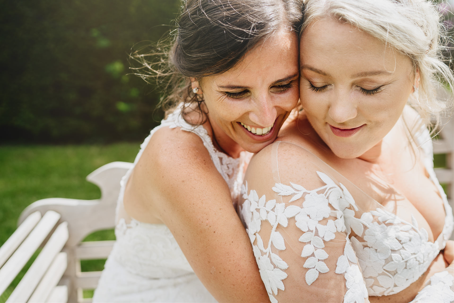 Two brides cuddling together on a bench in the sunshine