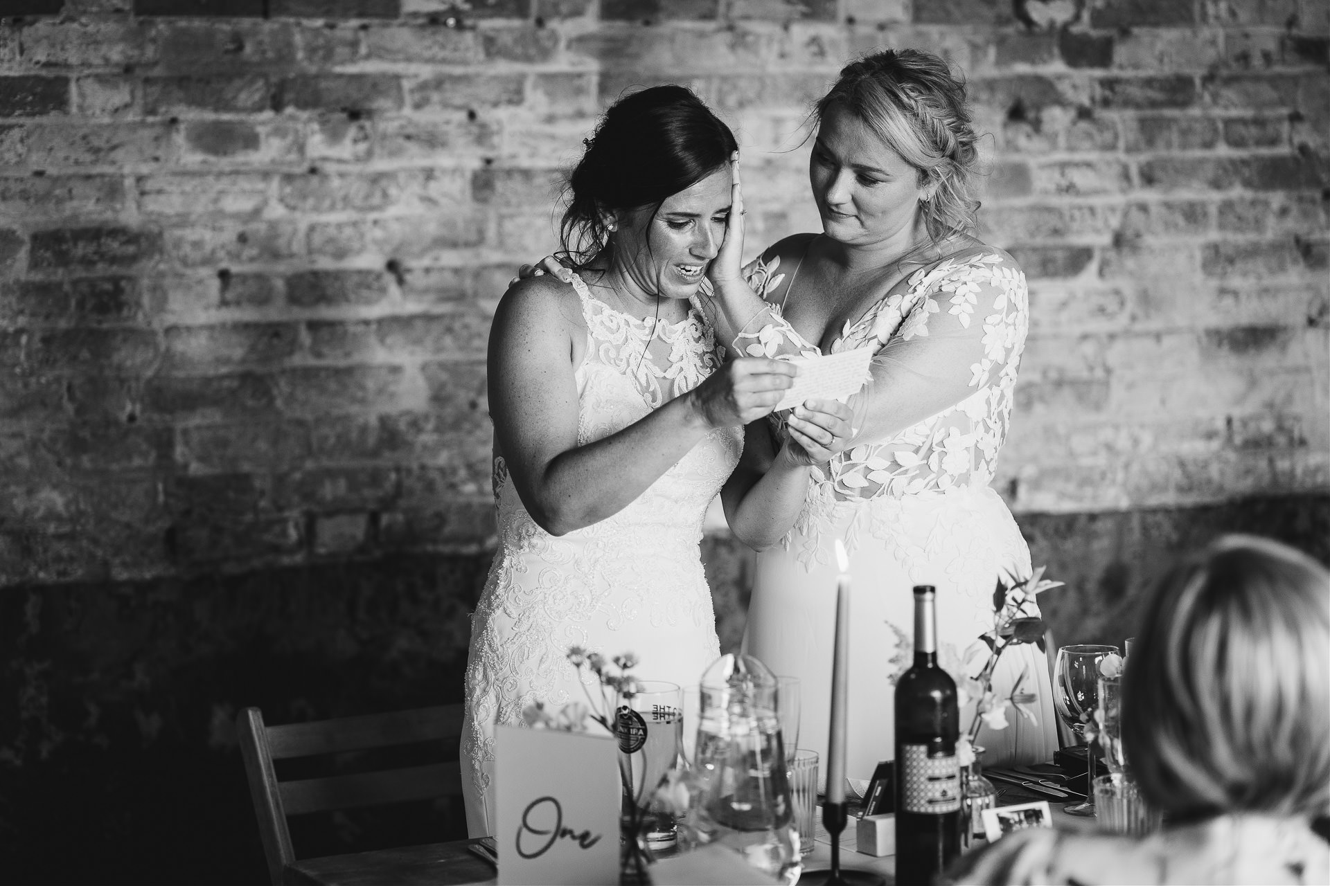 Bride holding her wife with a supportive hand on her face as she reads an emotional wedding speech