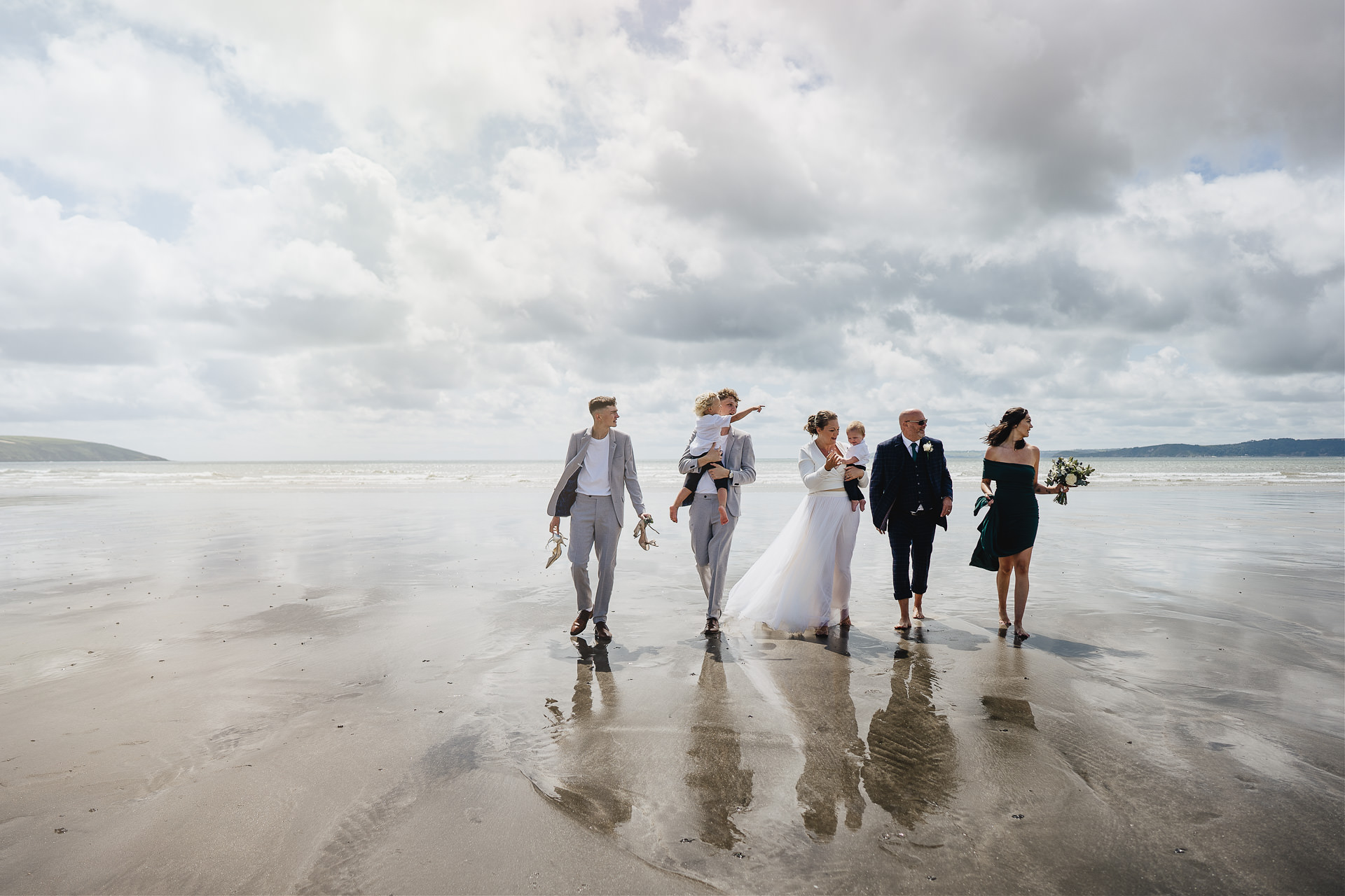 A bride and groom and family walking across a beach together
