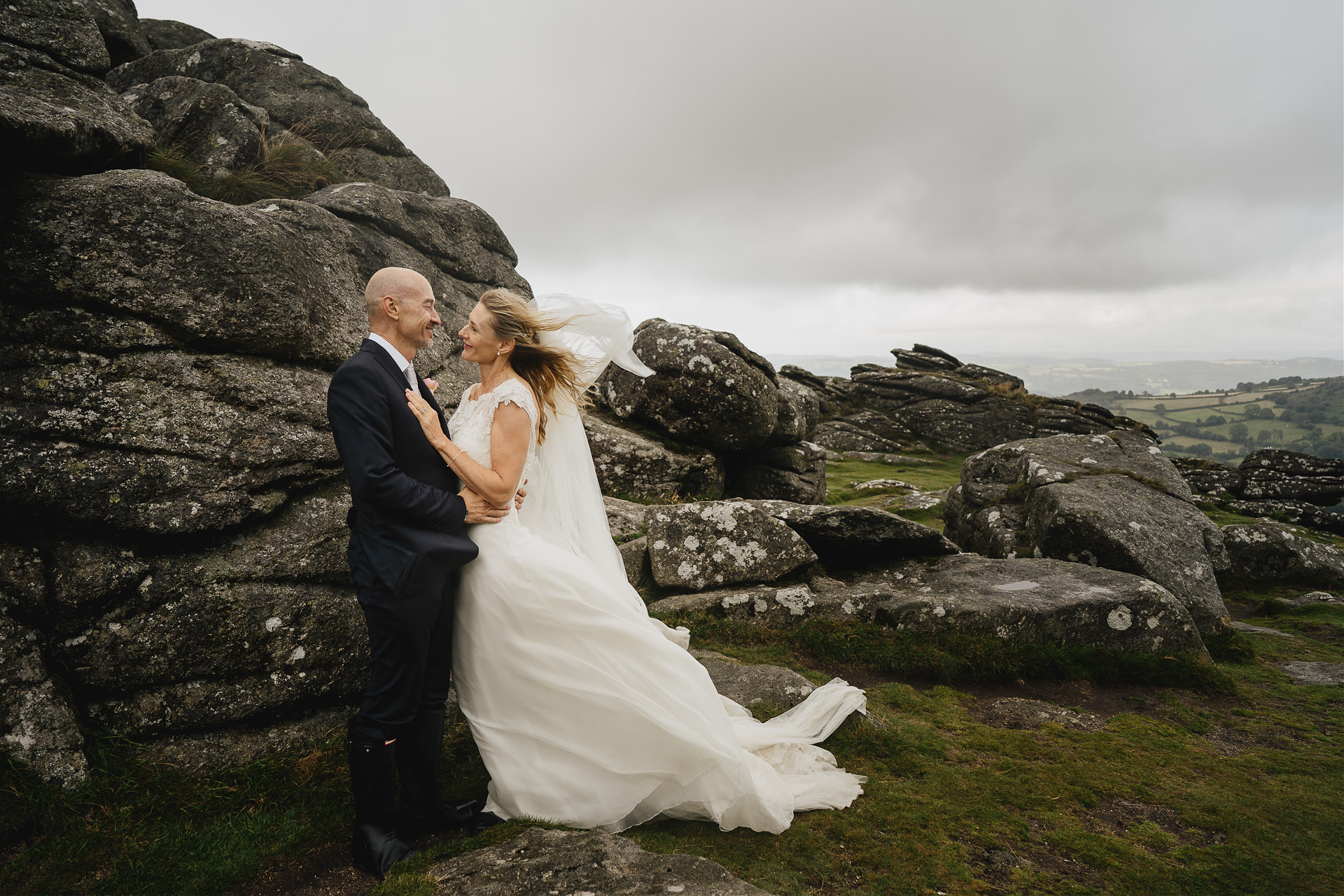 A bride and groom smiling at each other by the rocks at Hound Tor Dartmoor